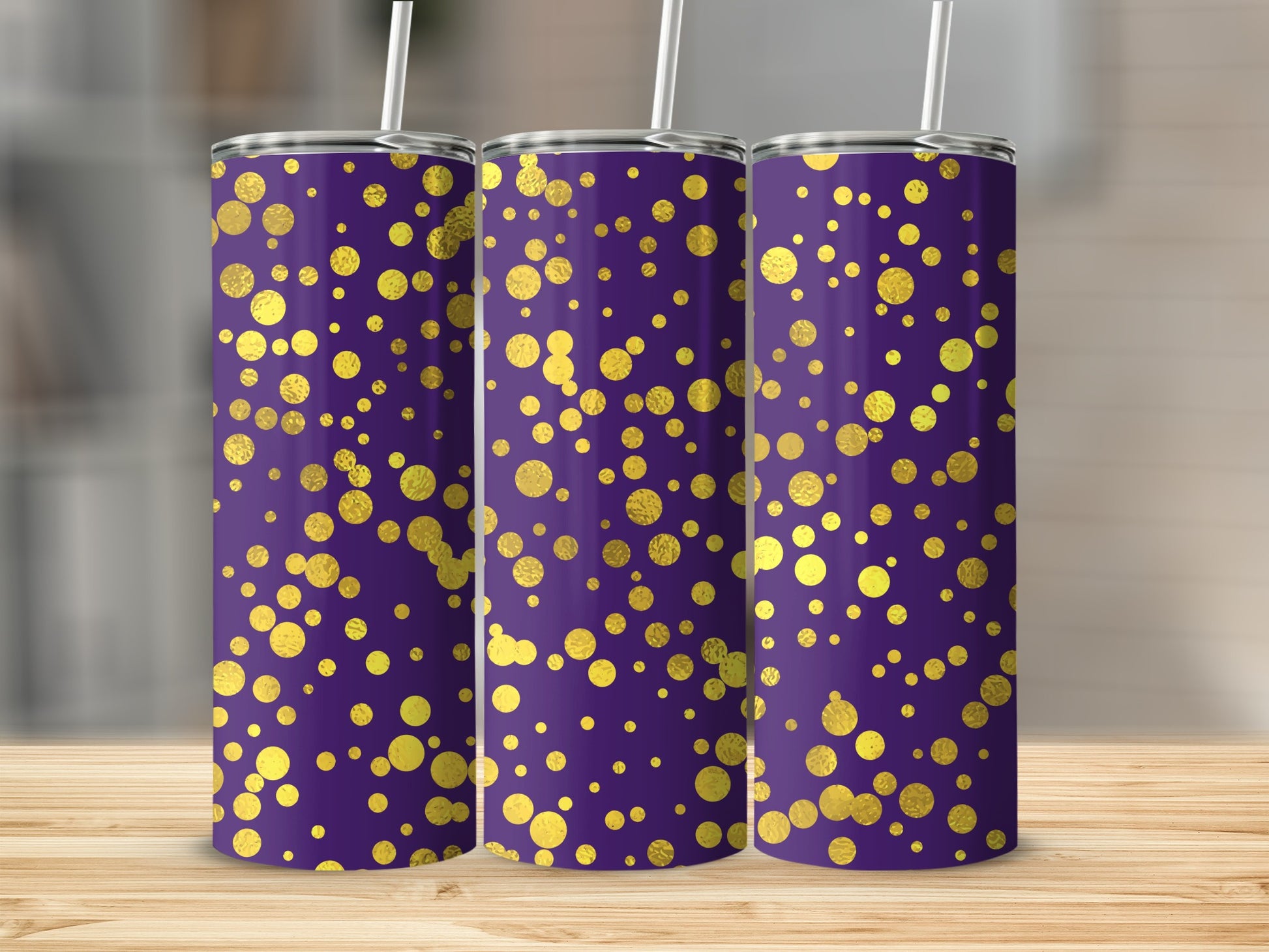Three purple tumblers with gold dot pattern and straw on wooden surface