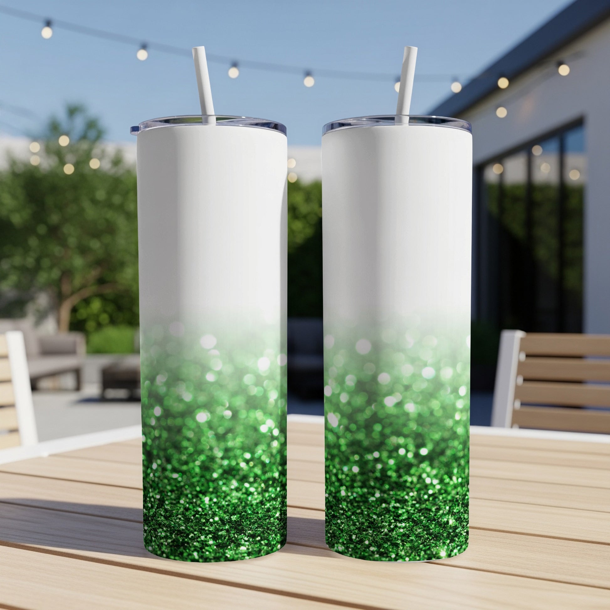 Two white tumblers with green glitter ombre design on outdoor table.