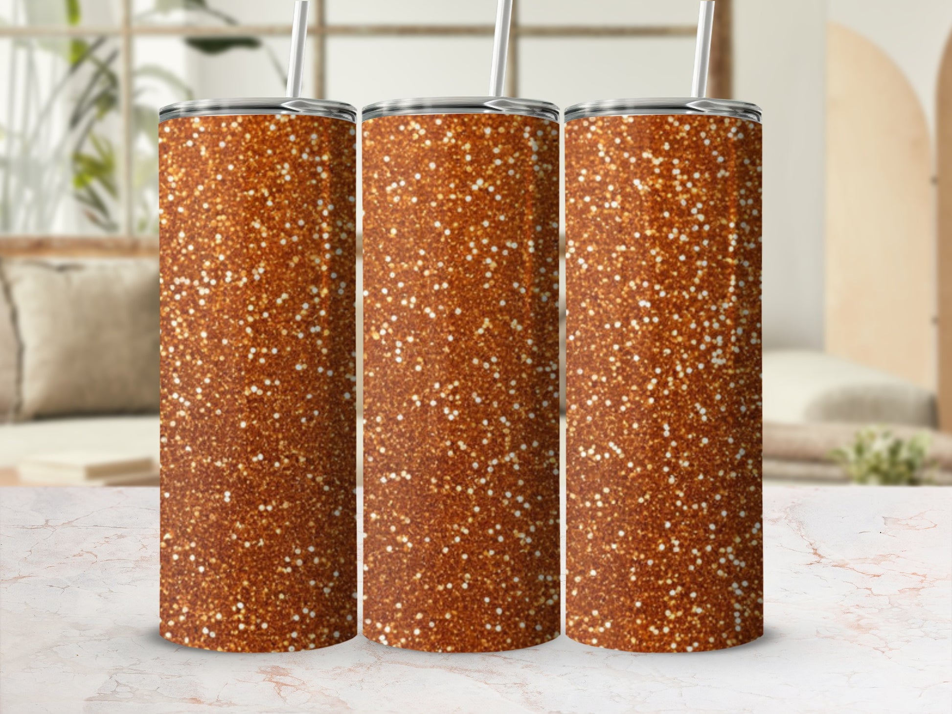 Three glitter-covered tumblers with straws on a marble surface.