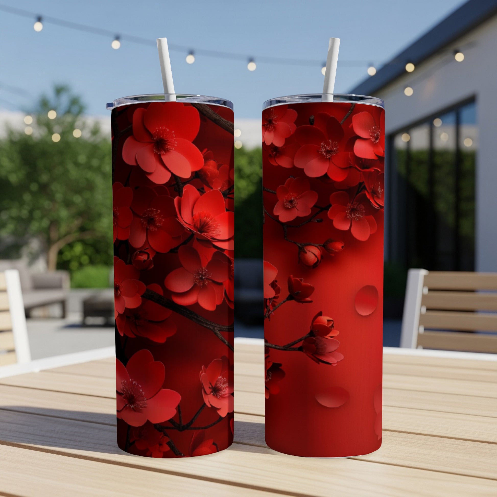 Two red floral tumblers with straws on a wooden table.