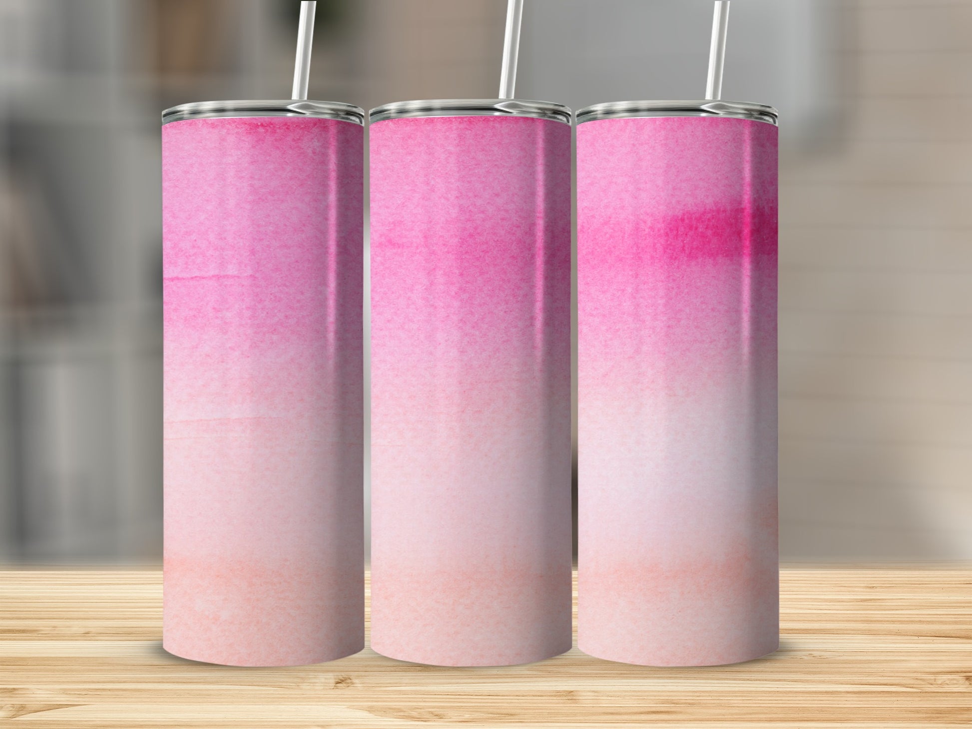 Three pink watercolor tumblers with straws on a wooden surface.