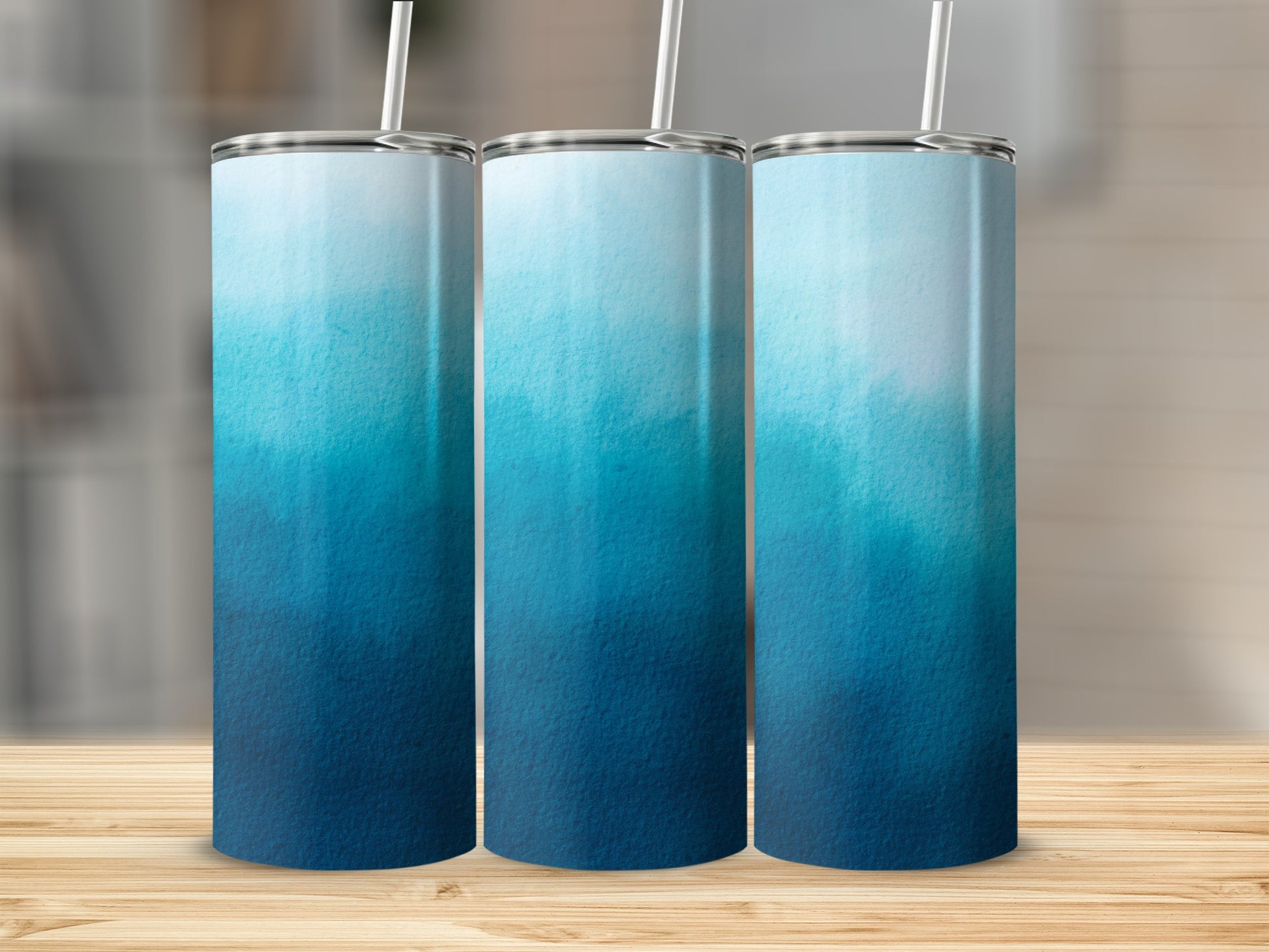 Three tumblers with a blue watercolor ombre design and straws.