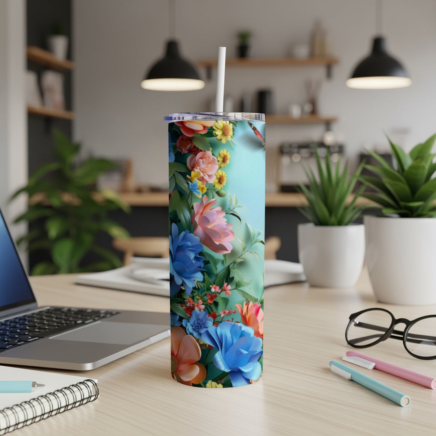 Floral tumbler with straw on a desk next to a laptop.