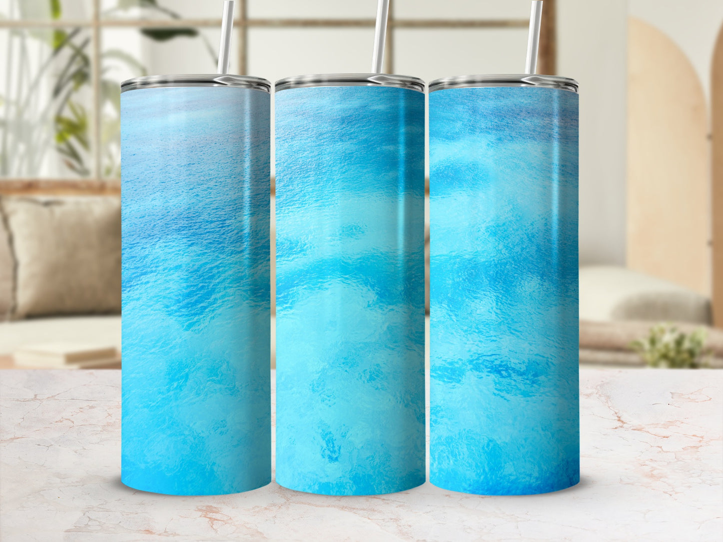 Three blue water textured tumblers with straws displayed on a marble surface.