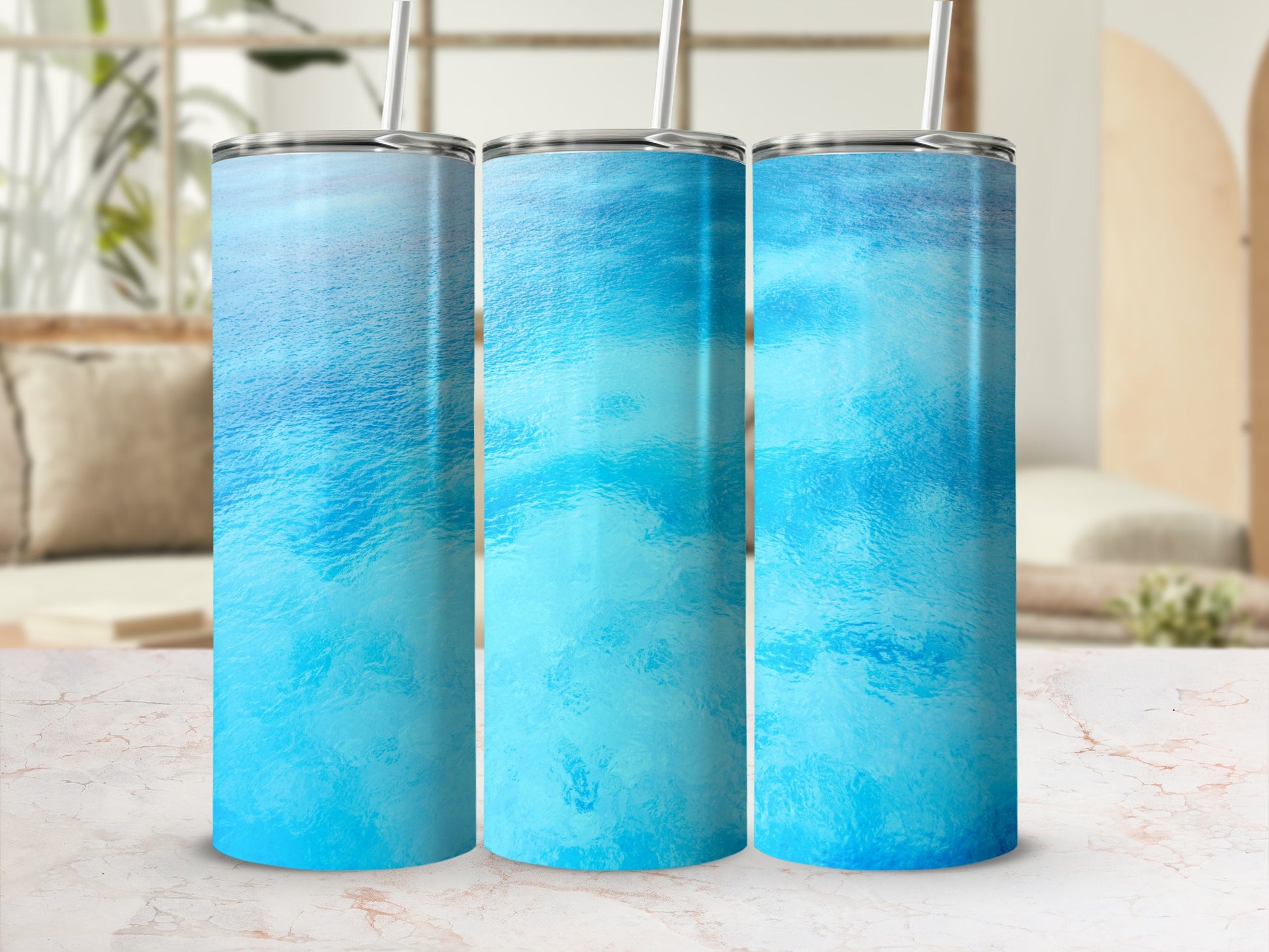 Three blue water textured tumblers with straws displayed on a marble surface.