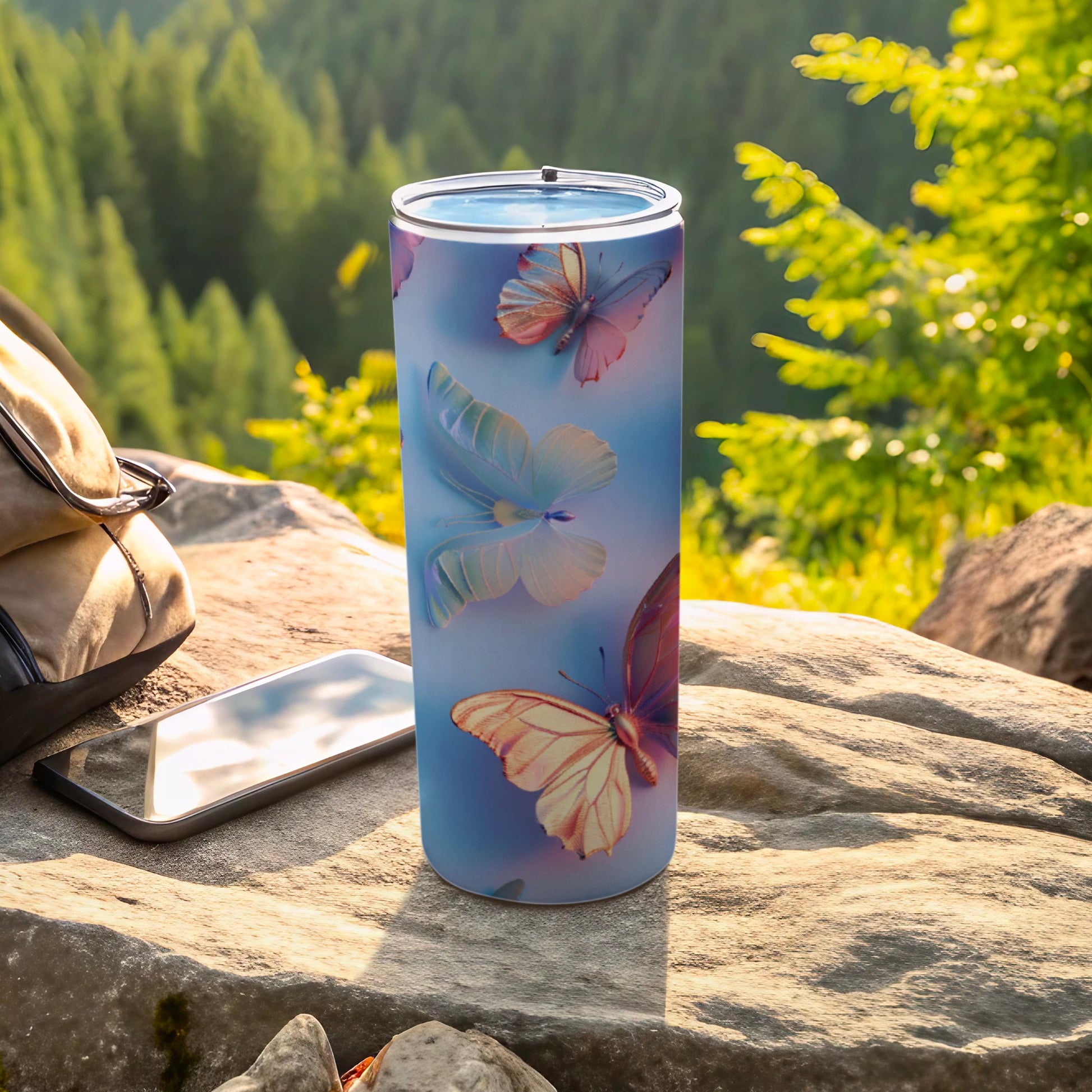 Blue tumbler with butterflies, a phone, and a backpack on rocks.