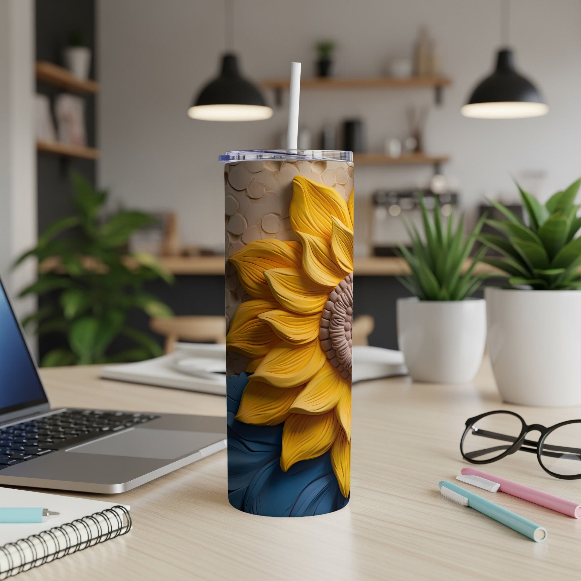 Tall tumbler with sunflower design and straw, on a desk.