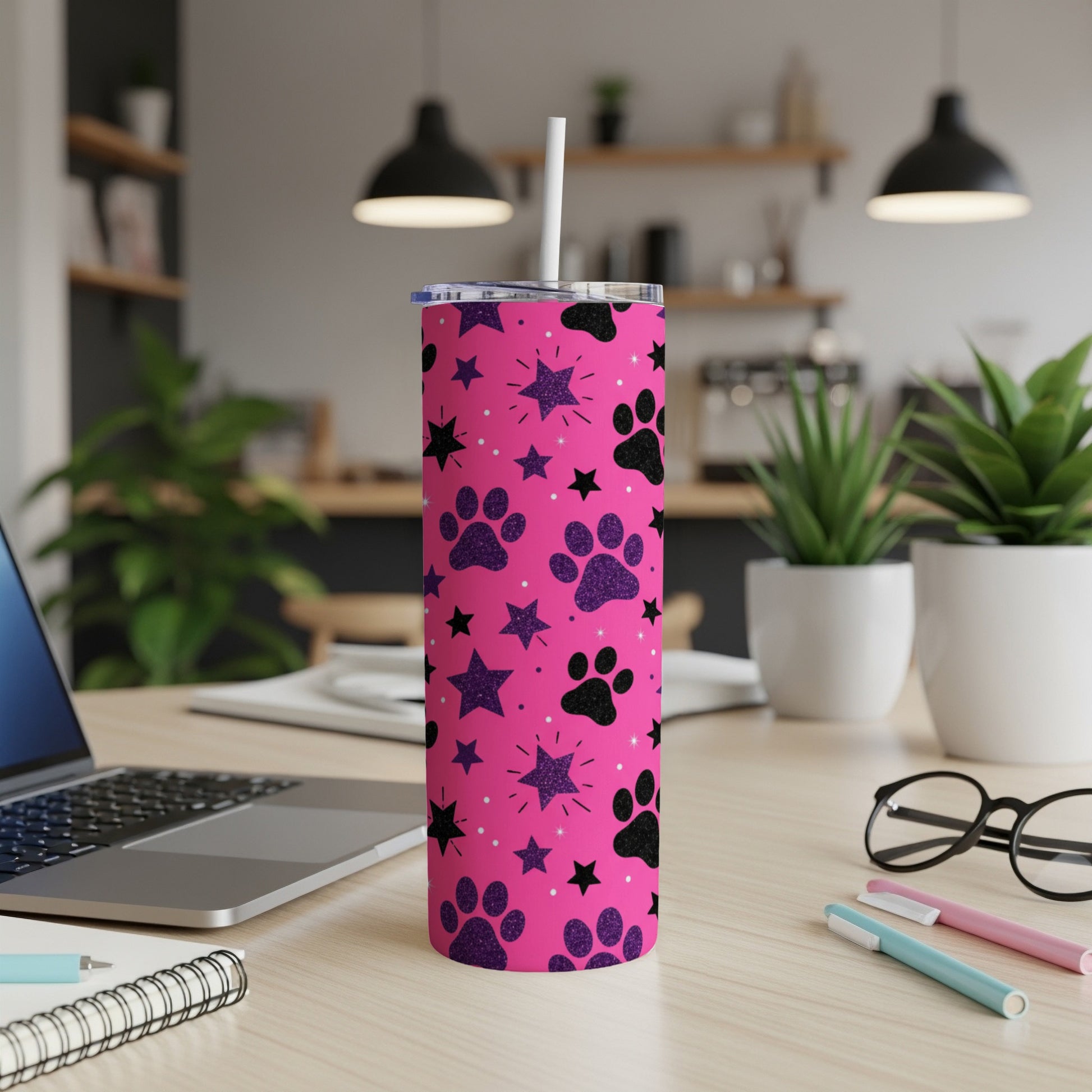 Pink tumbler with black paw prints and glitter stars, on a desk.