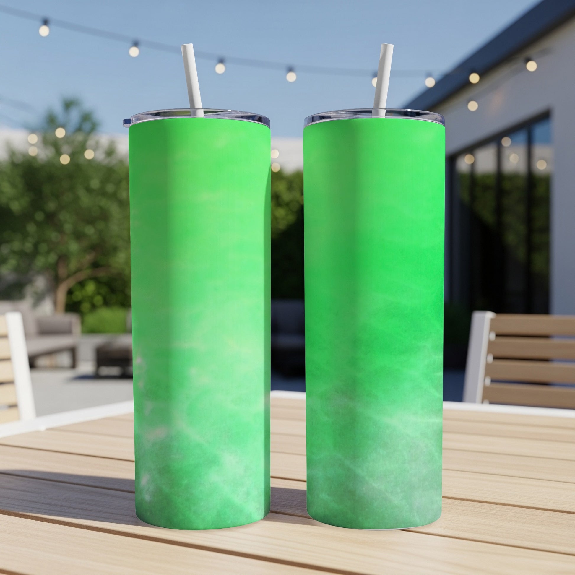 Two green tumblers with straws on a wooden table outdoors.