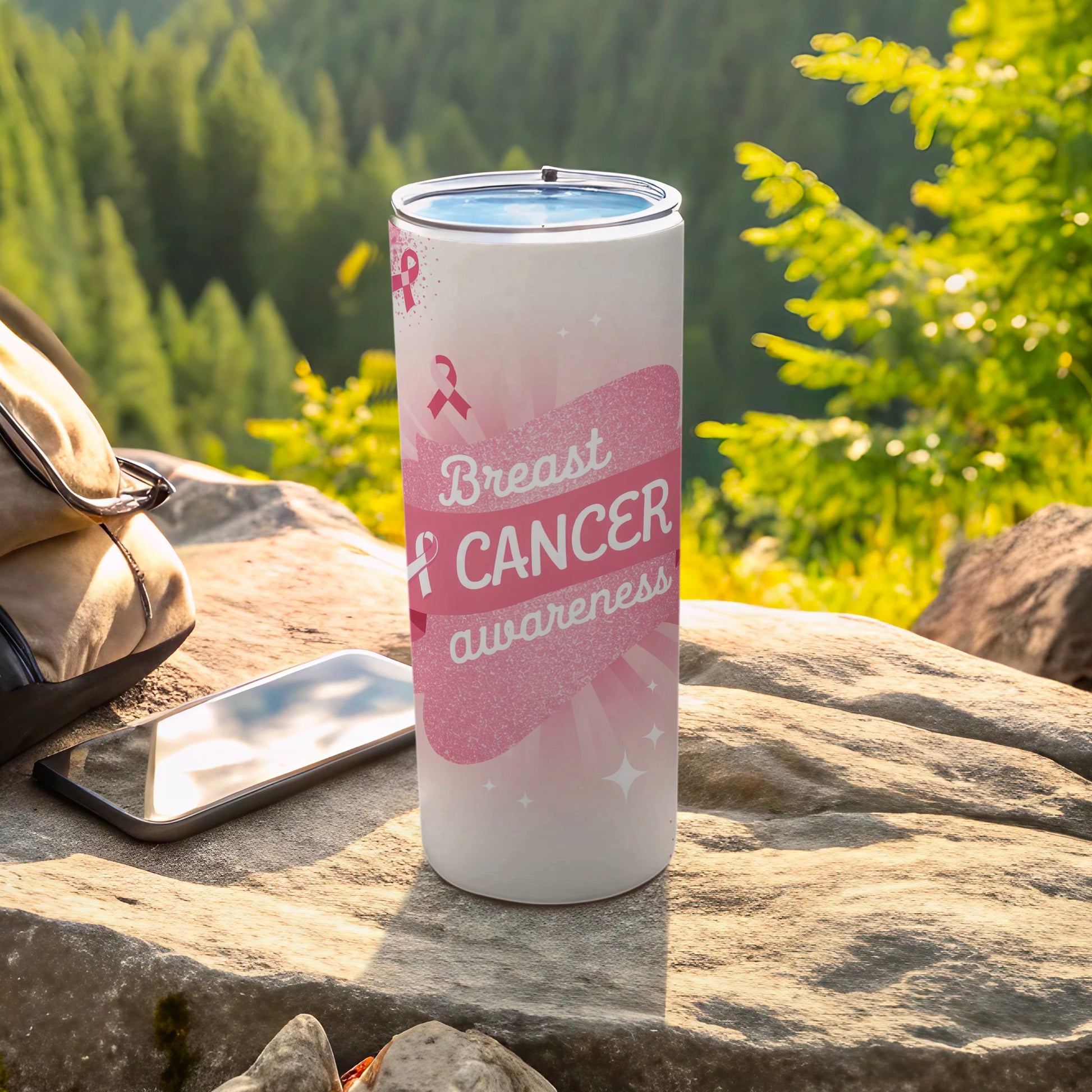 White tumbler with pink ribbon, "Breast Cancer awareness" text, on rocky terrain.