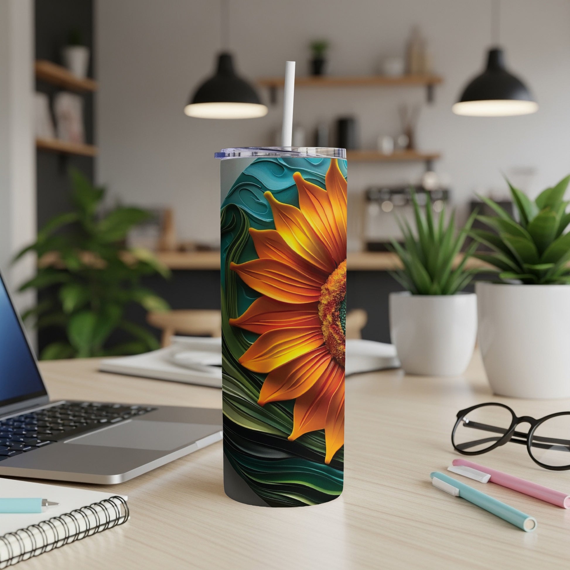 Sunflower tumbler with straw on a desk, with laptop and plants.
