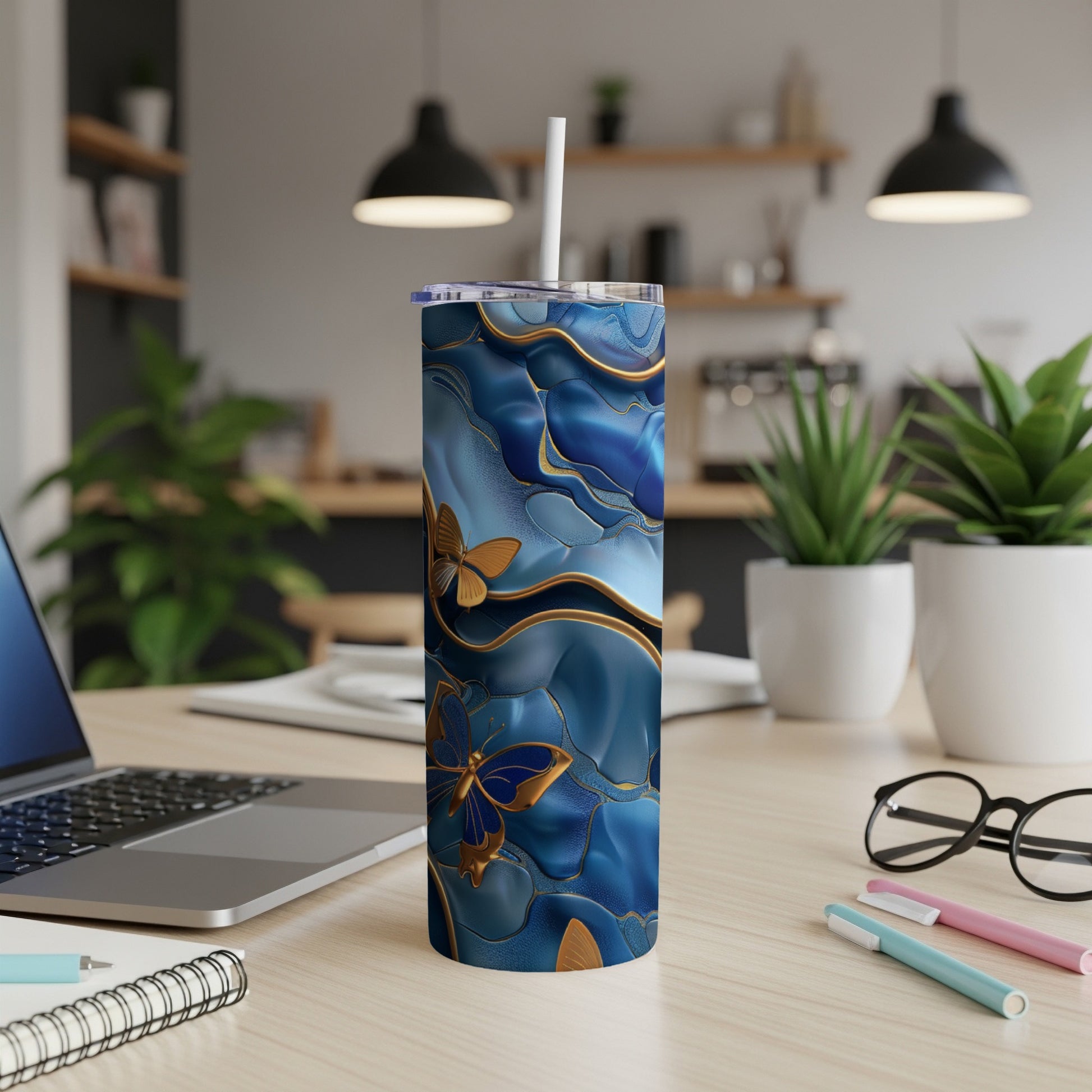 Blue and gold abstract butterfly patterned skinny tumbler with straw on desk.