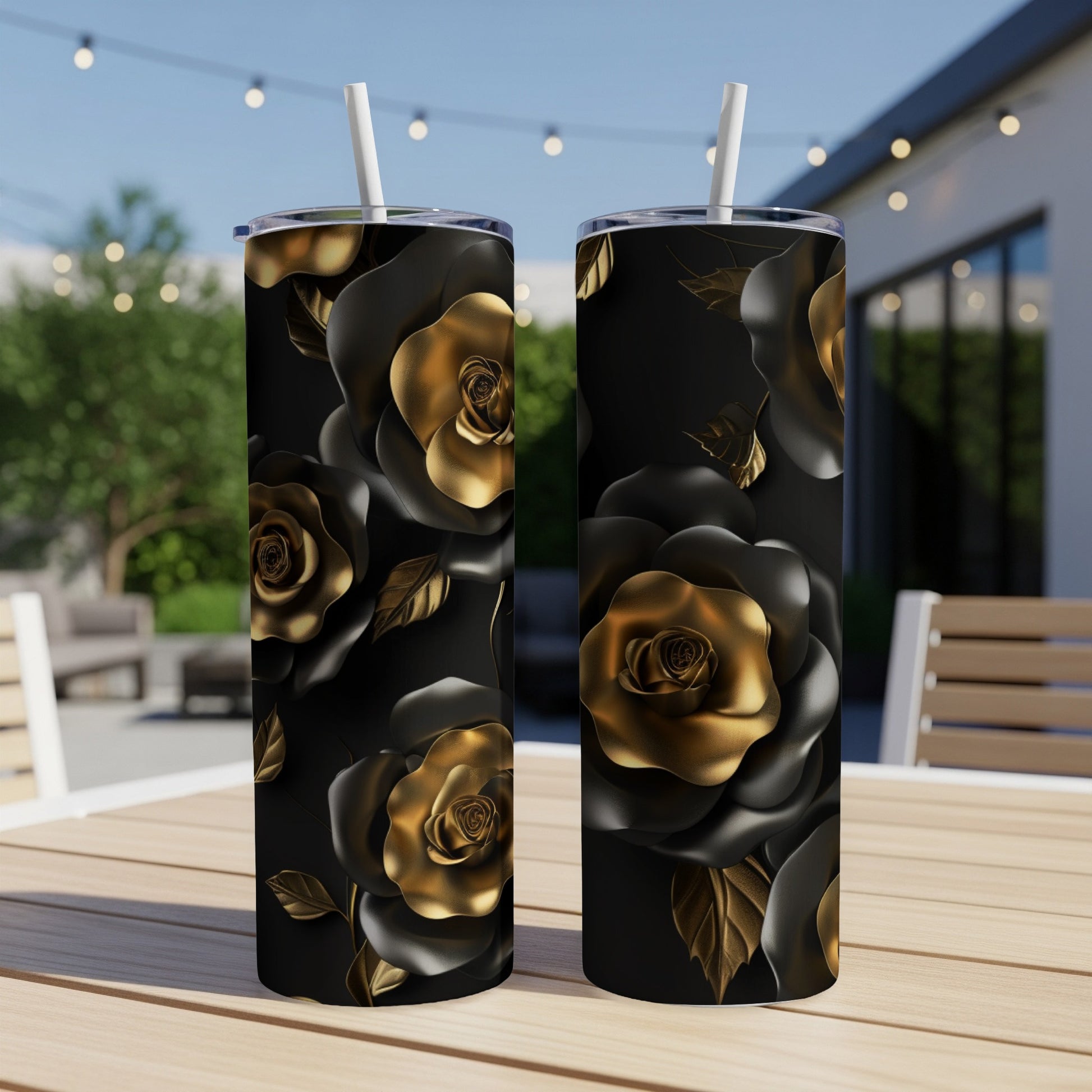 Two black tumblers with gold rose pattern and straws on a wooden table.