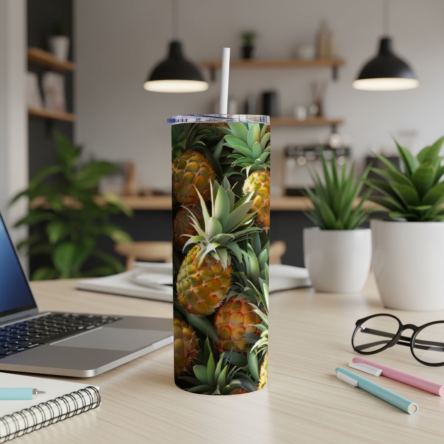 Tall tumbler with pineapple pattern and a straw on a desk.
