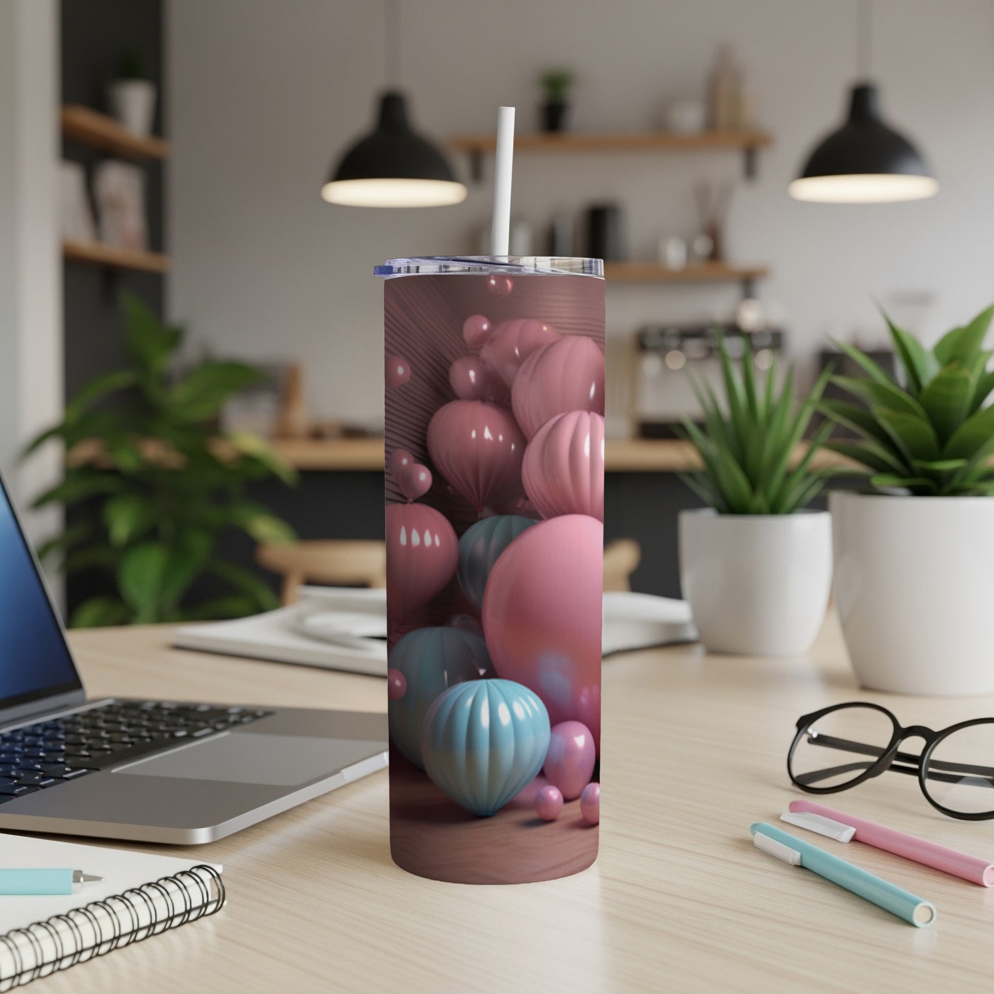 Pink and blue balloons on a tumbler with a straw, on a desk.