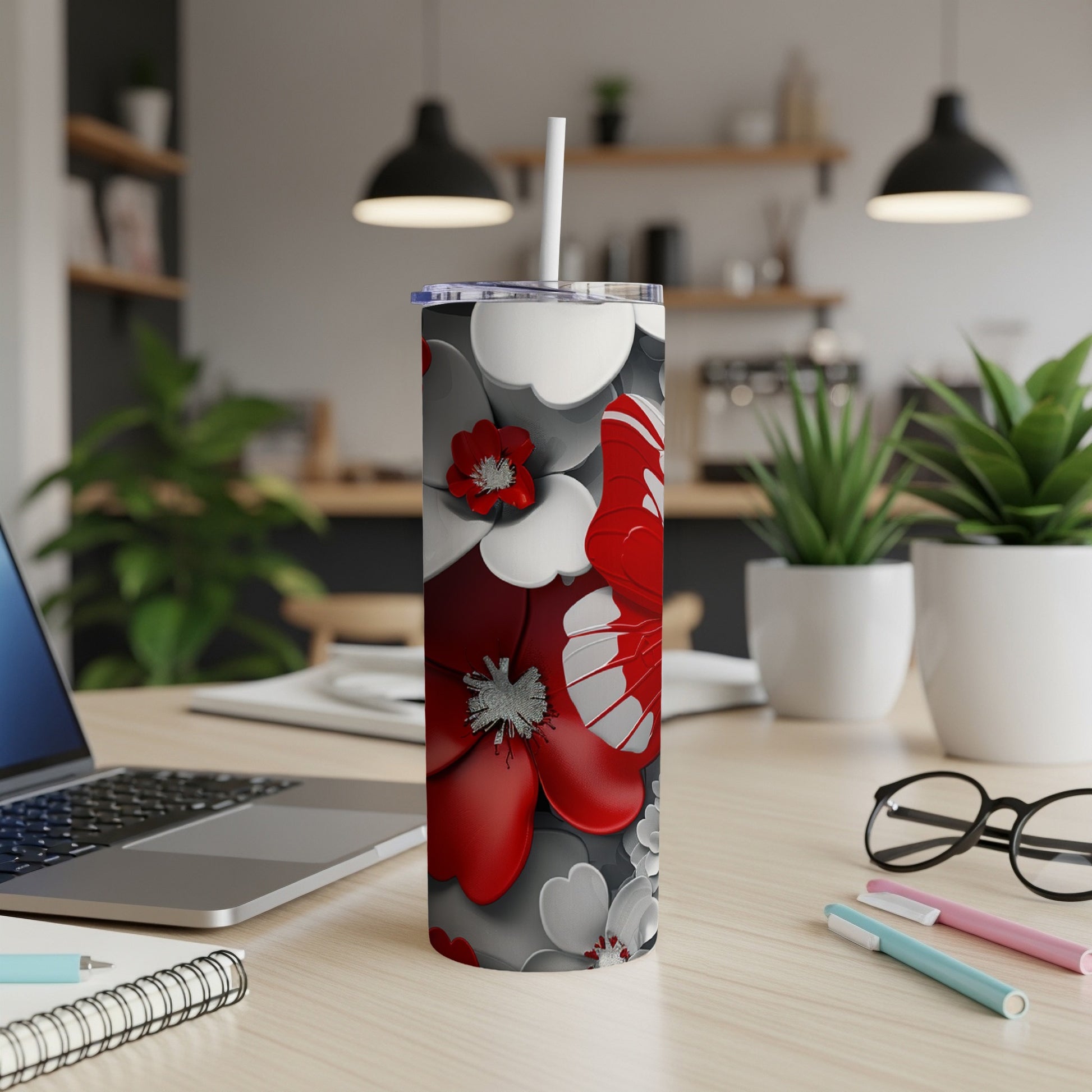 Red and white floral pattern on a white tumbler with straw, on a desk.