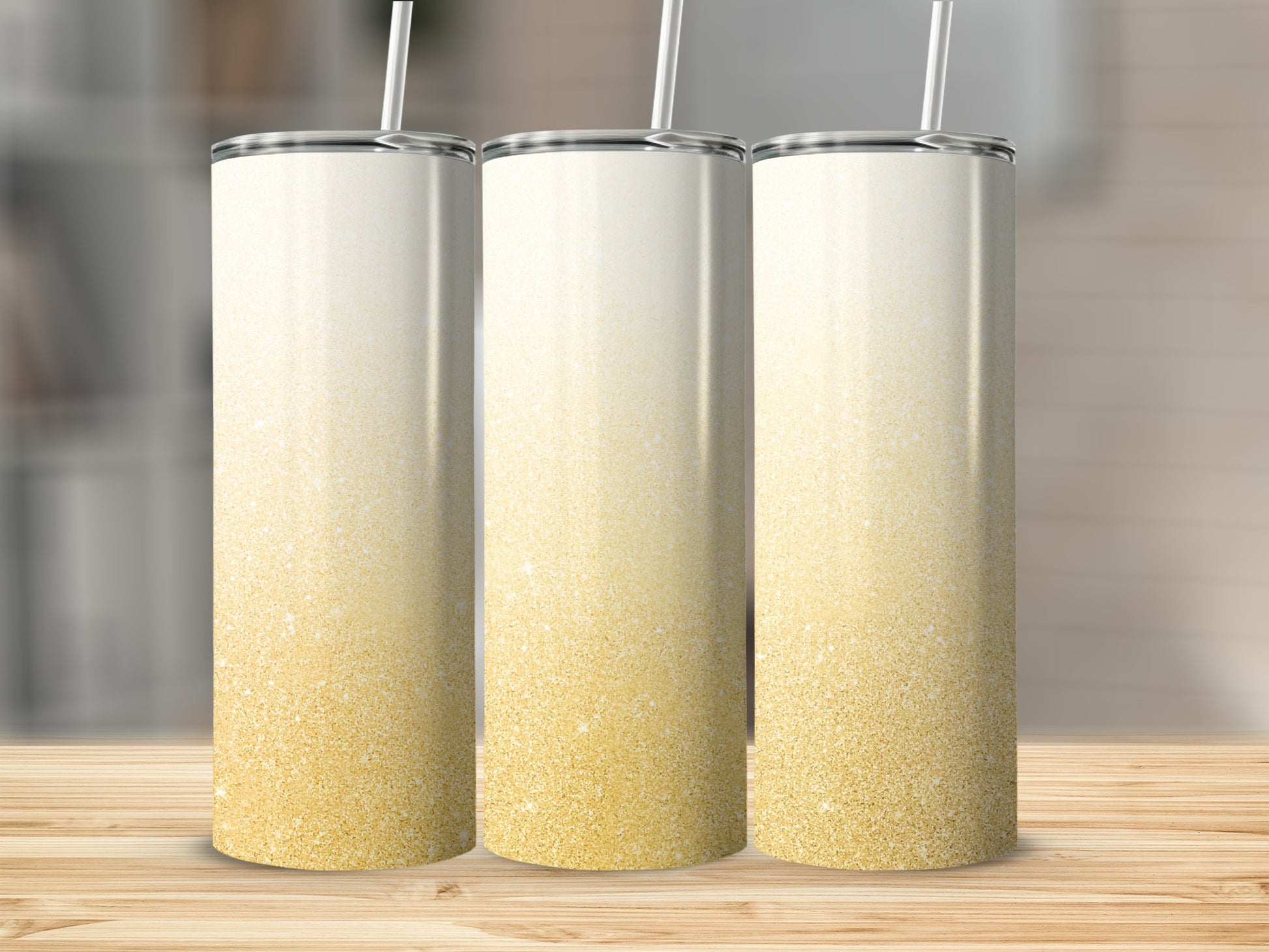 Three tall, glittery tumblers with straws on a wooden surface.