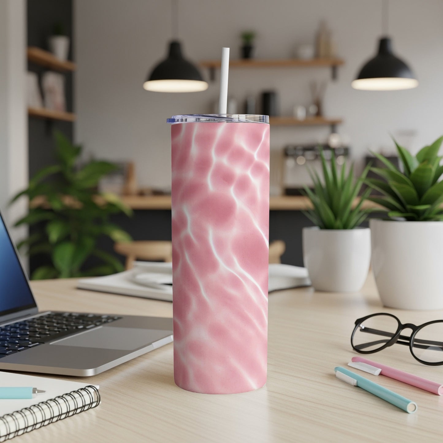 Pink marble tumbler with straw on desk with laptop and plants.