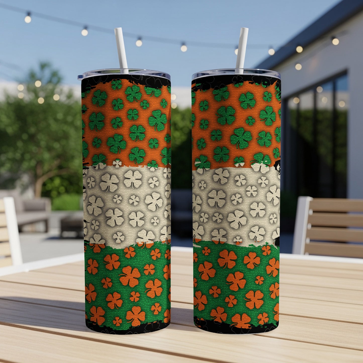 Two tumblers with green, orange, and white shamrock patterns on a table outdoors.