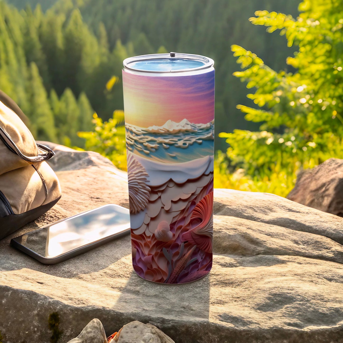 Tall tumbler with beach scene design rests on rocks near phone and backpack.