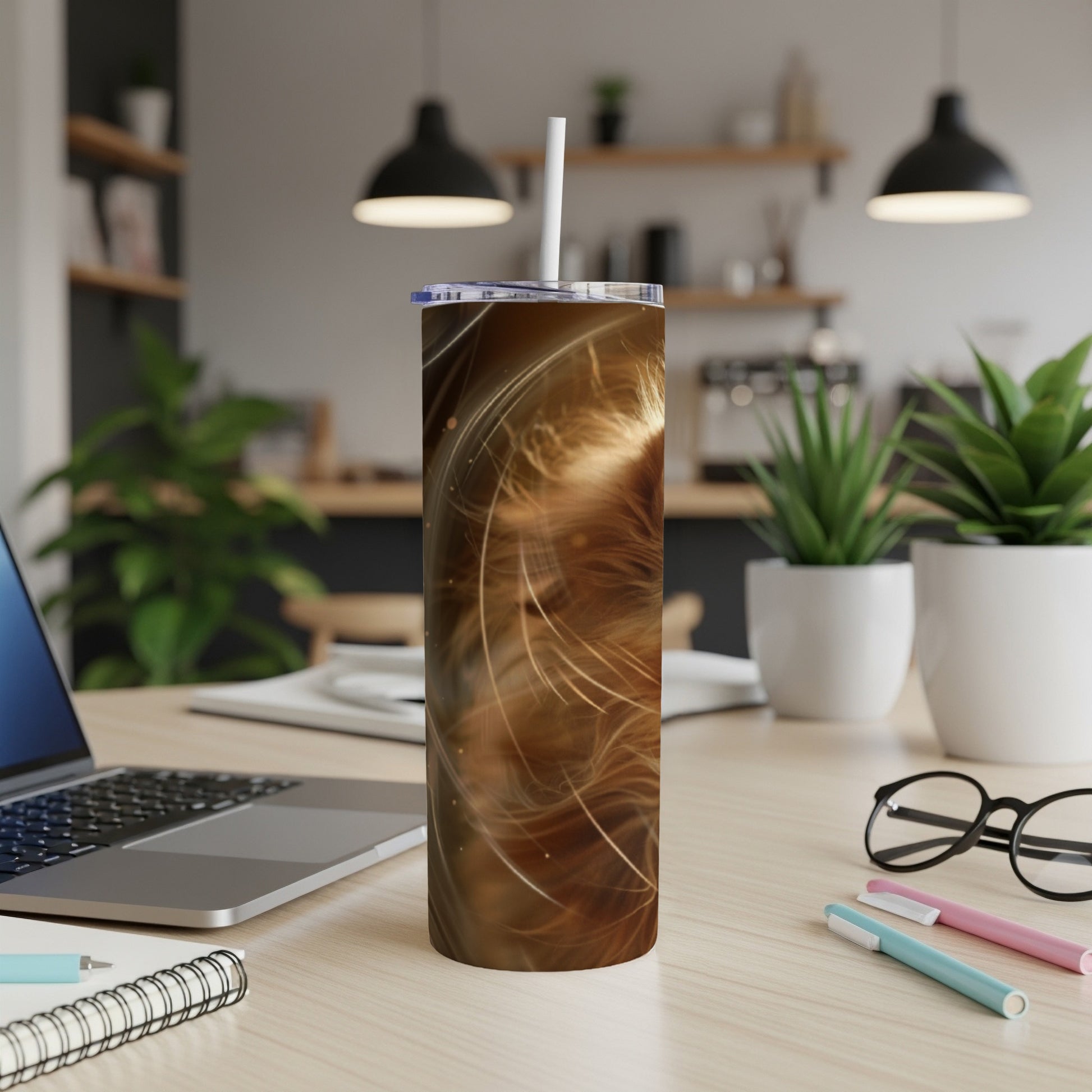Brown speckled tumbler with straw on a desk with a laptop and pens.