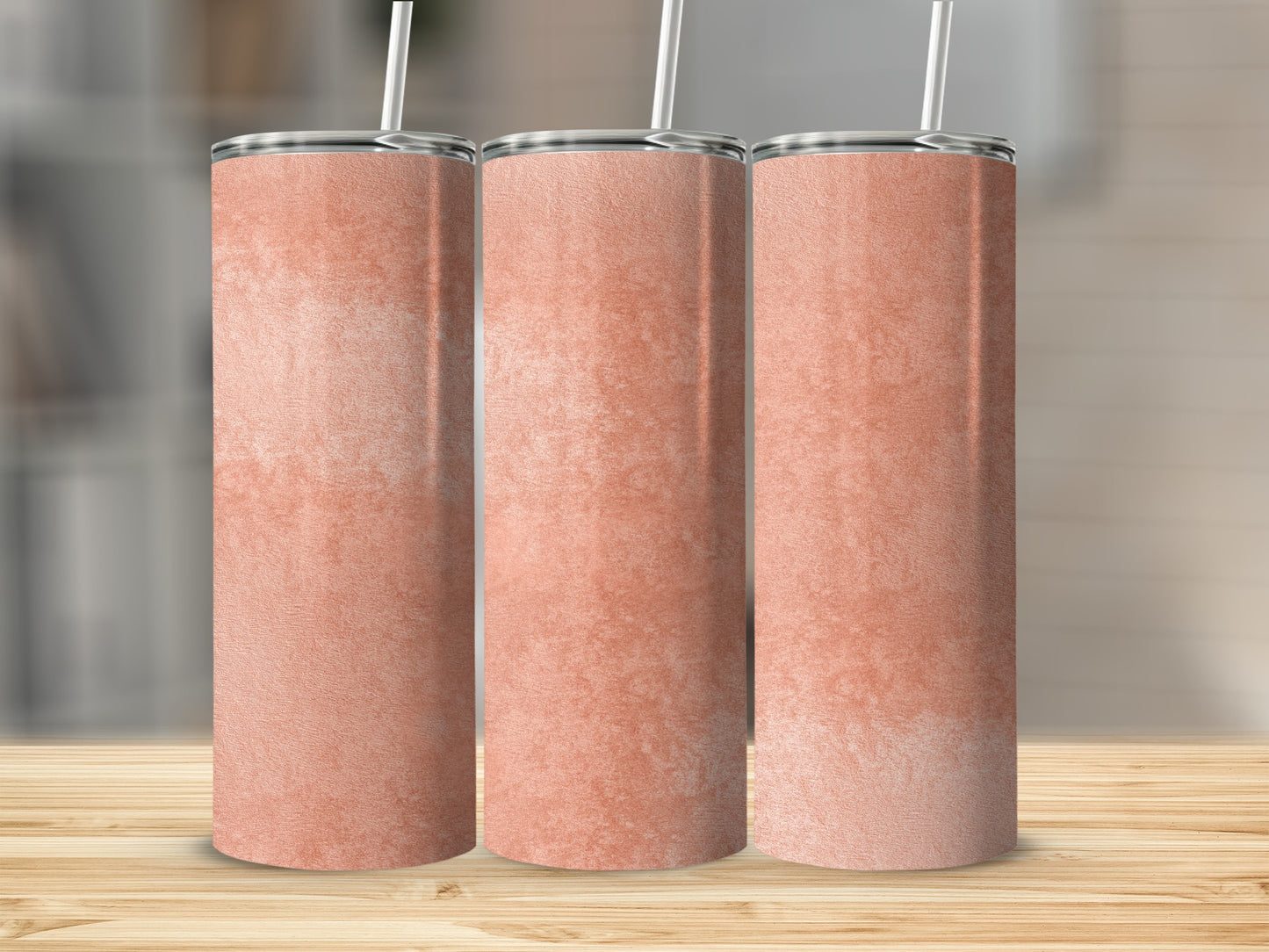 Three blank coral tumblers with straws on a wooden surface.