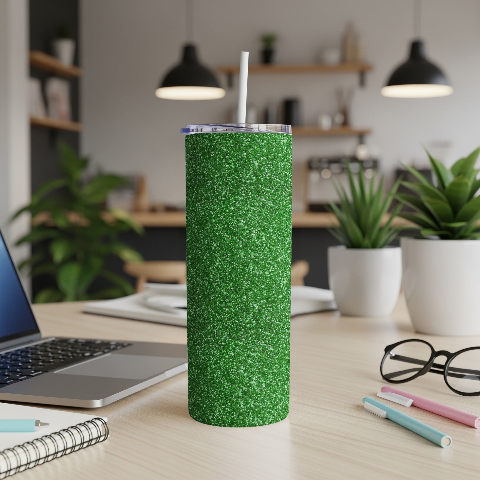 Green glitter tumbler with a straw on a wooden desk.