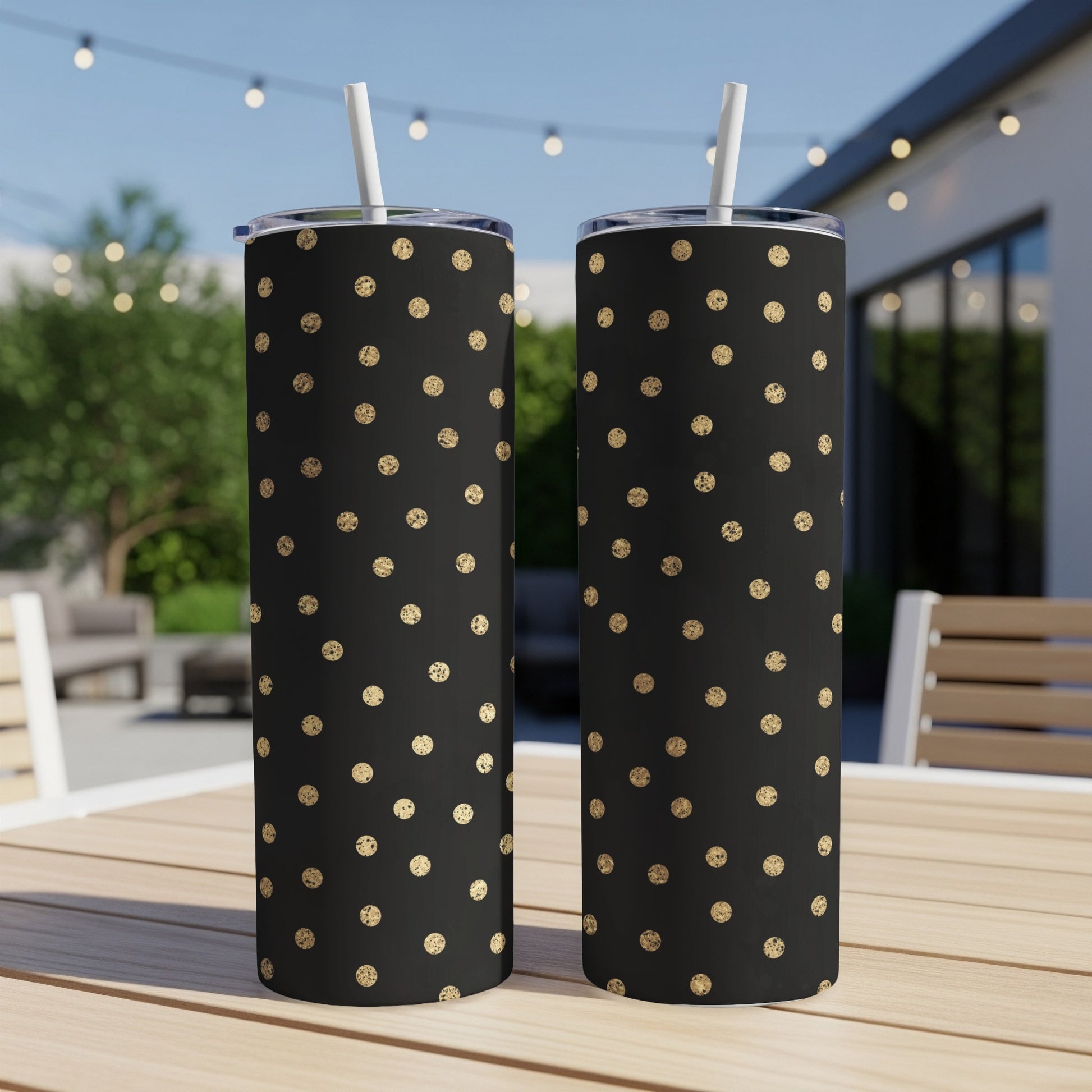 Two black tumblers with gold polka dots and white straws sit on a table.