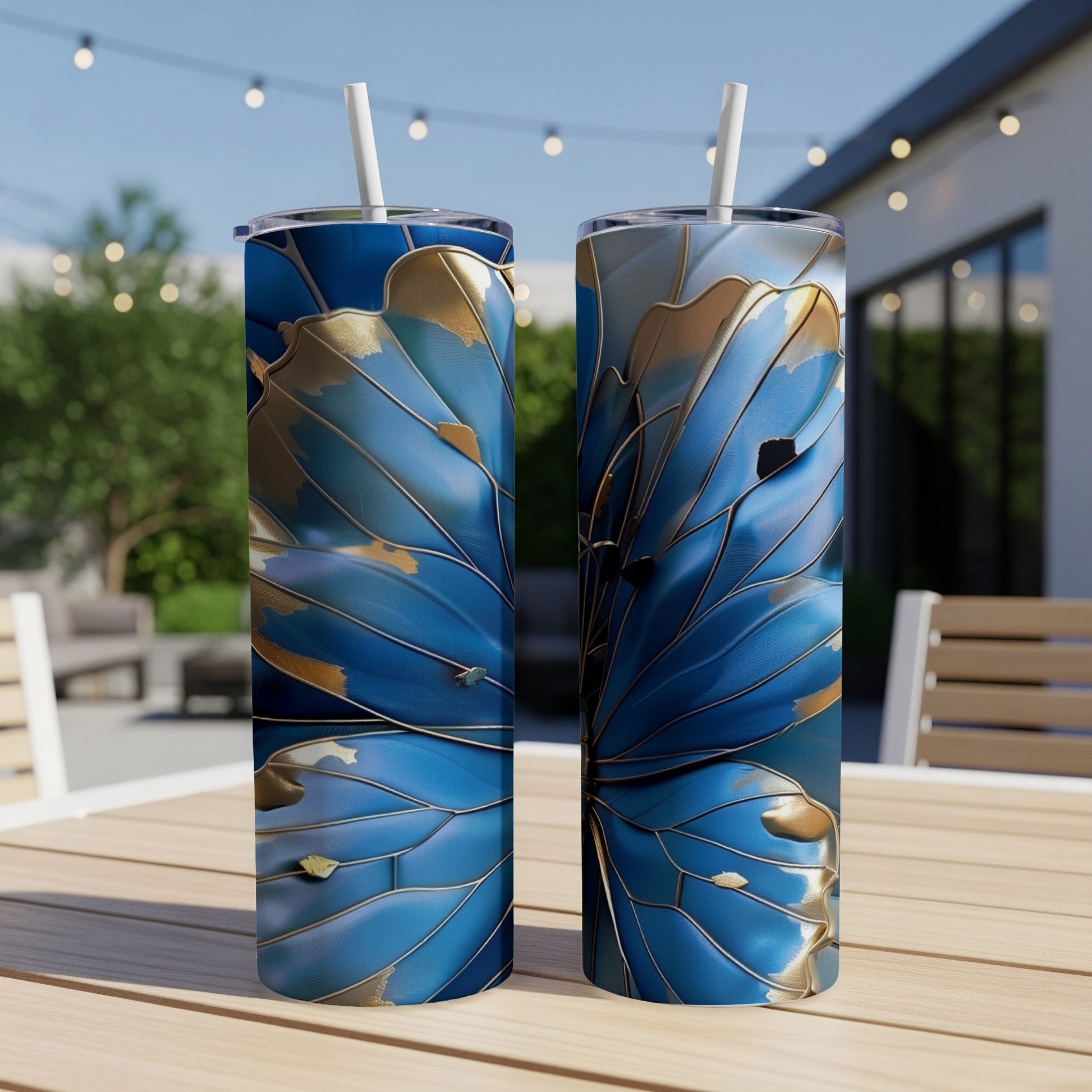 Two blue and gold abstract floral pattern tumblers with straws on a wooden table.