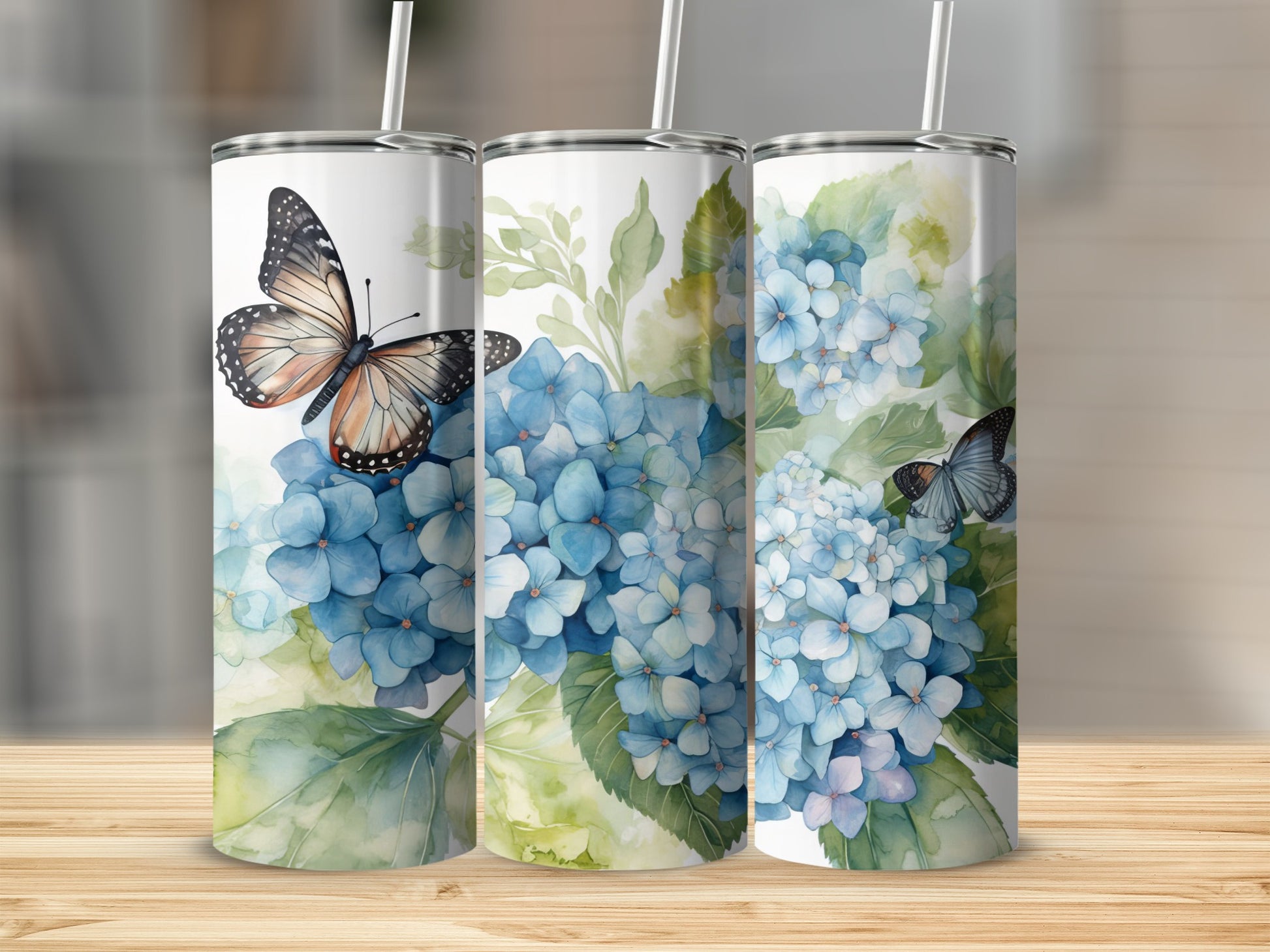 Three tumblers featuring blue hydrangeas and butterflies, displayed on a wooden surface.