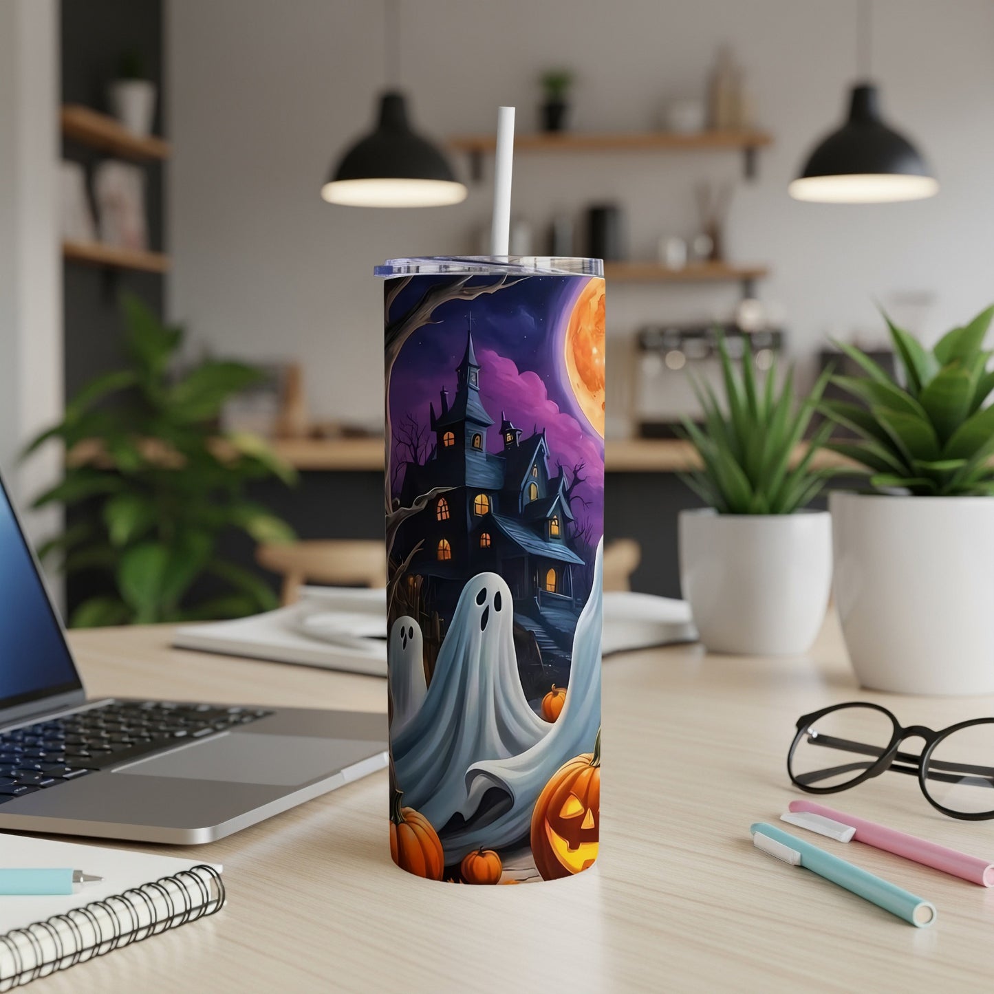 Halloween tumbler with haunted house, ghosts, and pumpkins, on a desk.