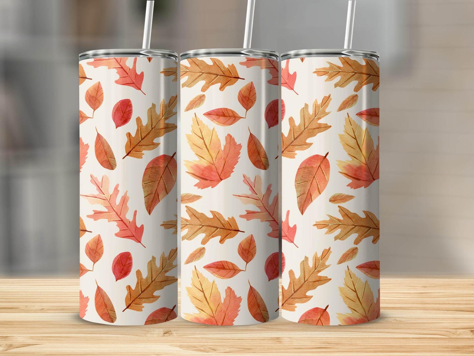 Three tumblers with a watercolor fall leaf pattern on a wooden surface.