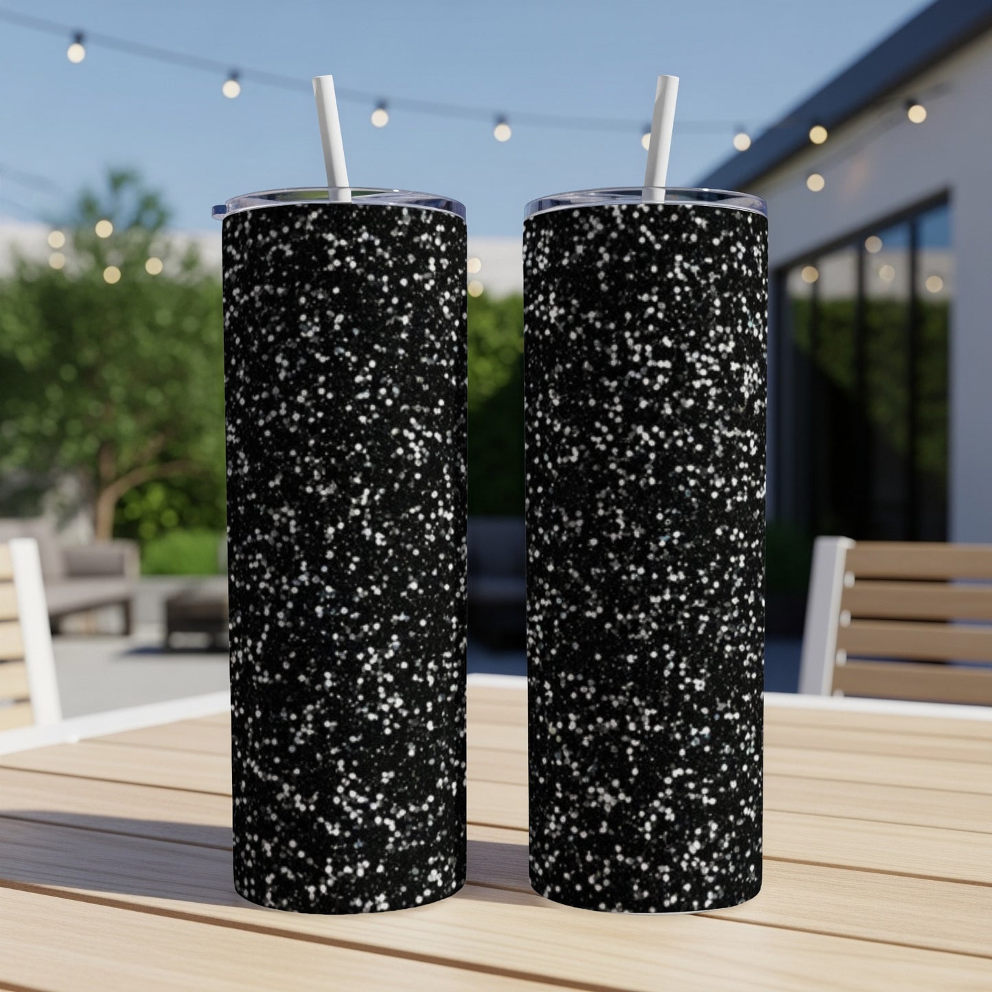 Two black glitter tumblers with white straws on a table.