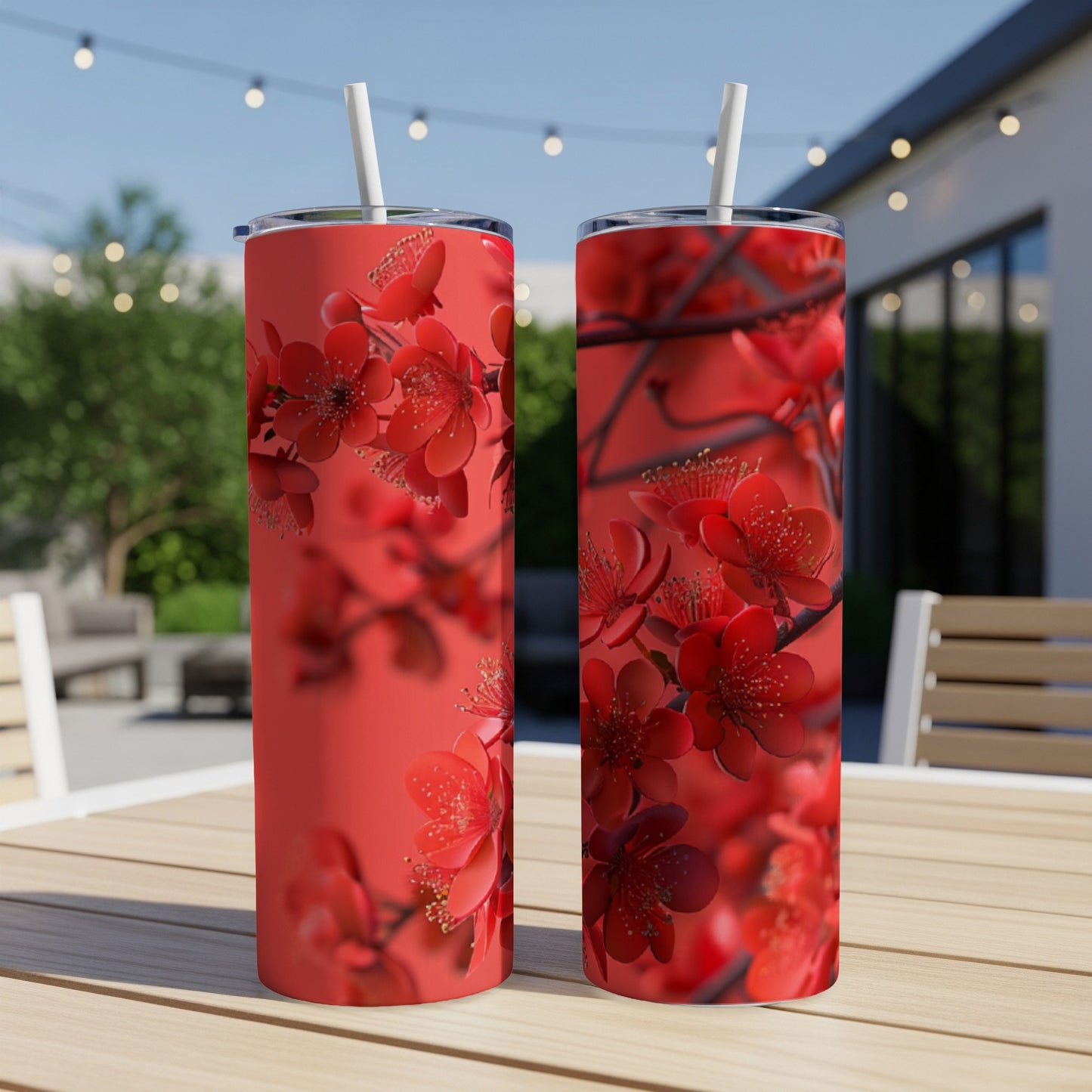 Red cherry blossoms adorn two identical tumblers with straws on a wooden table.