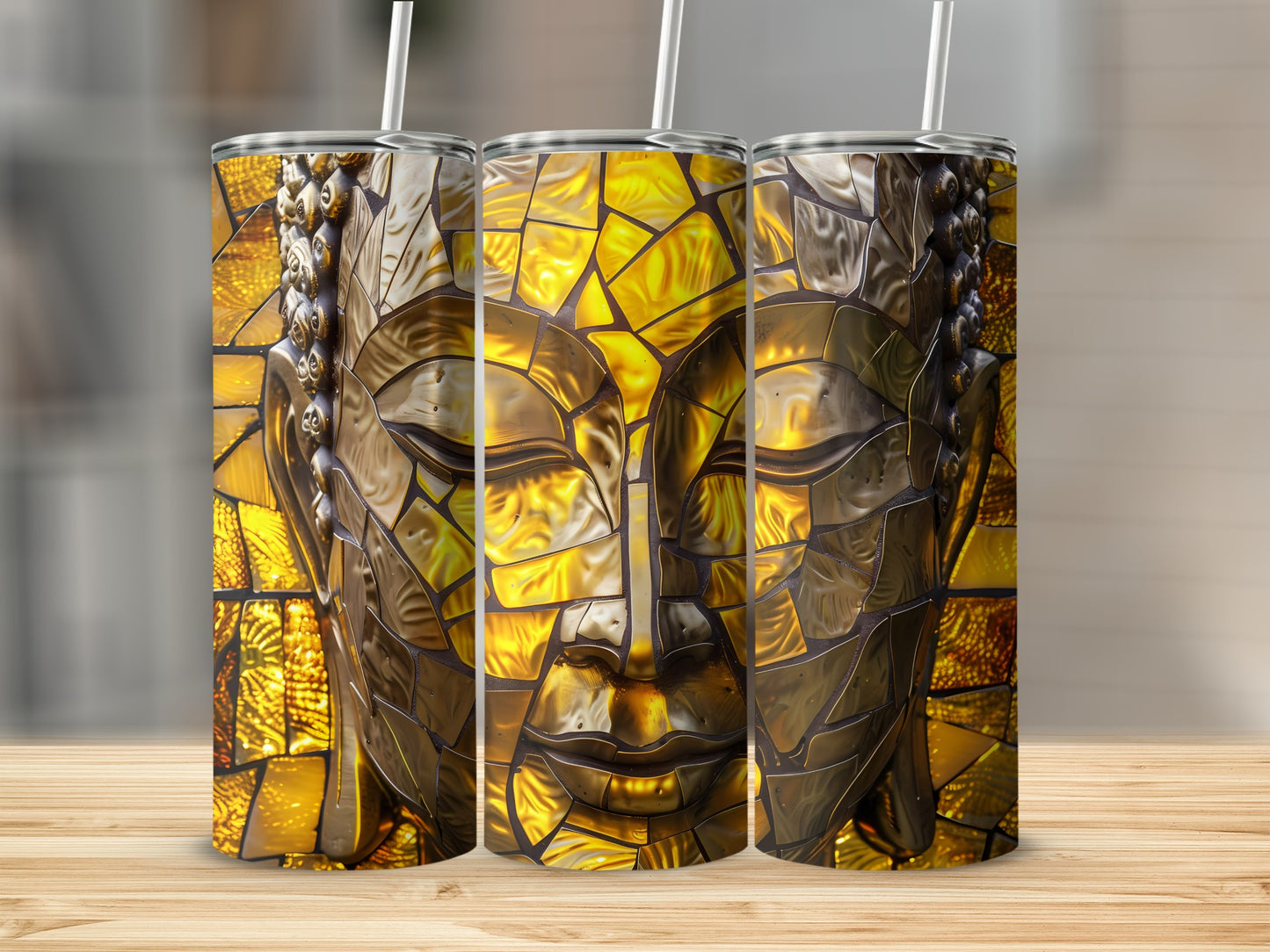 Three gold mosaic Buddha face tumblers with straws on a wooden surface.