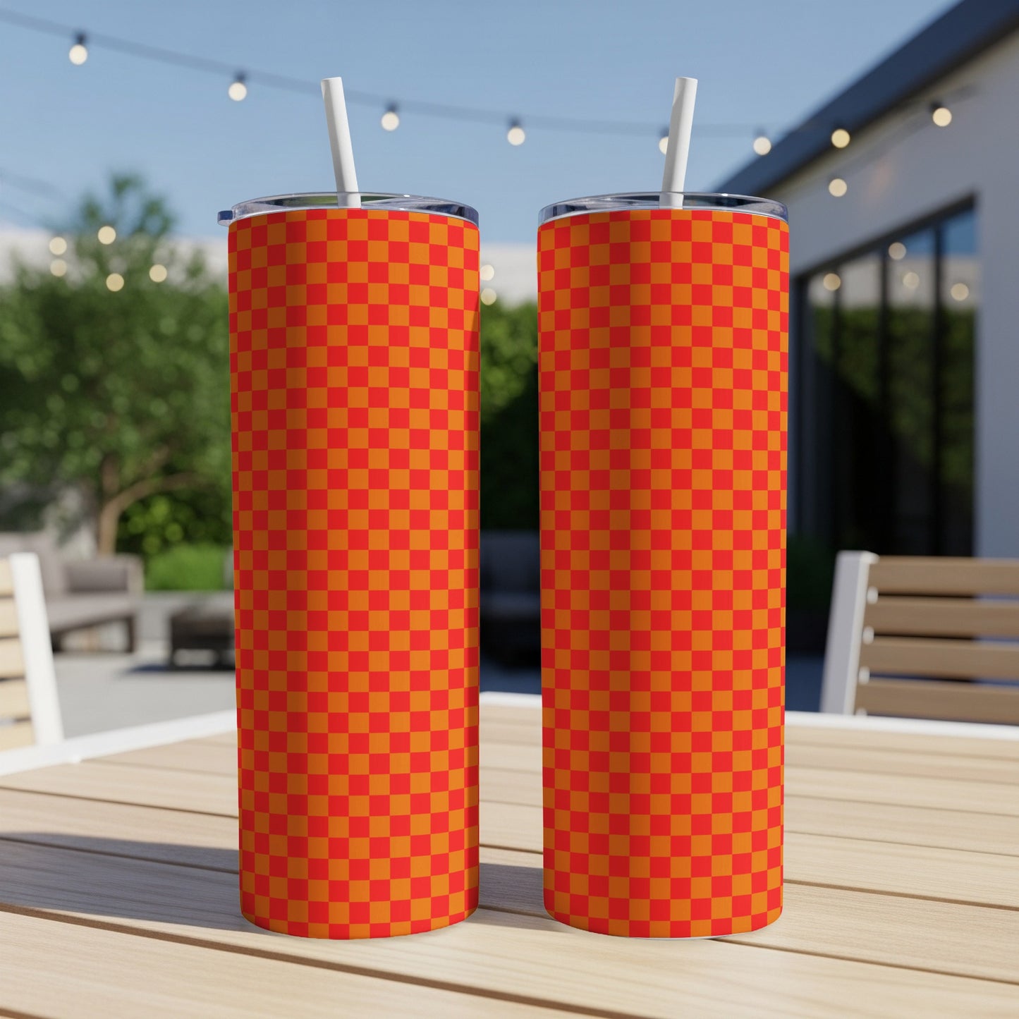 Two tall orange and red checkered tumblers with straws on a wooden table.