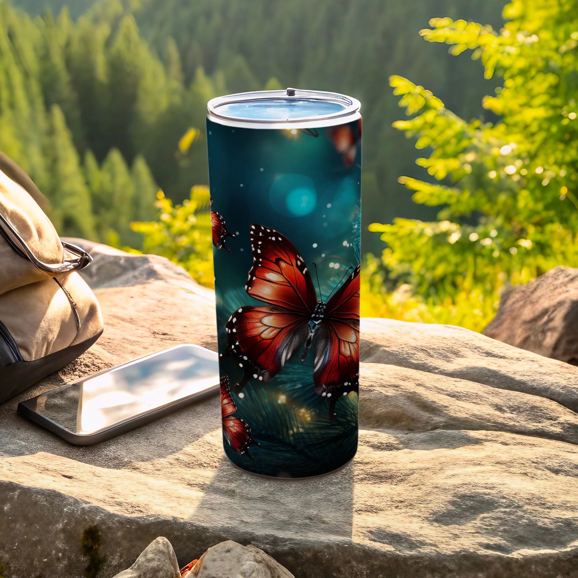 Red butterfly pattern on a stainless steel tumbler with a phone and bag.