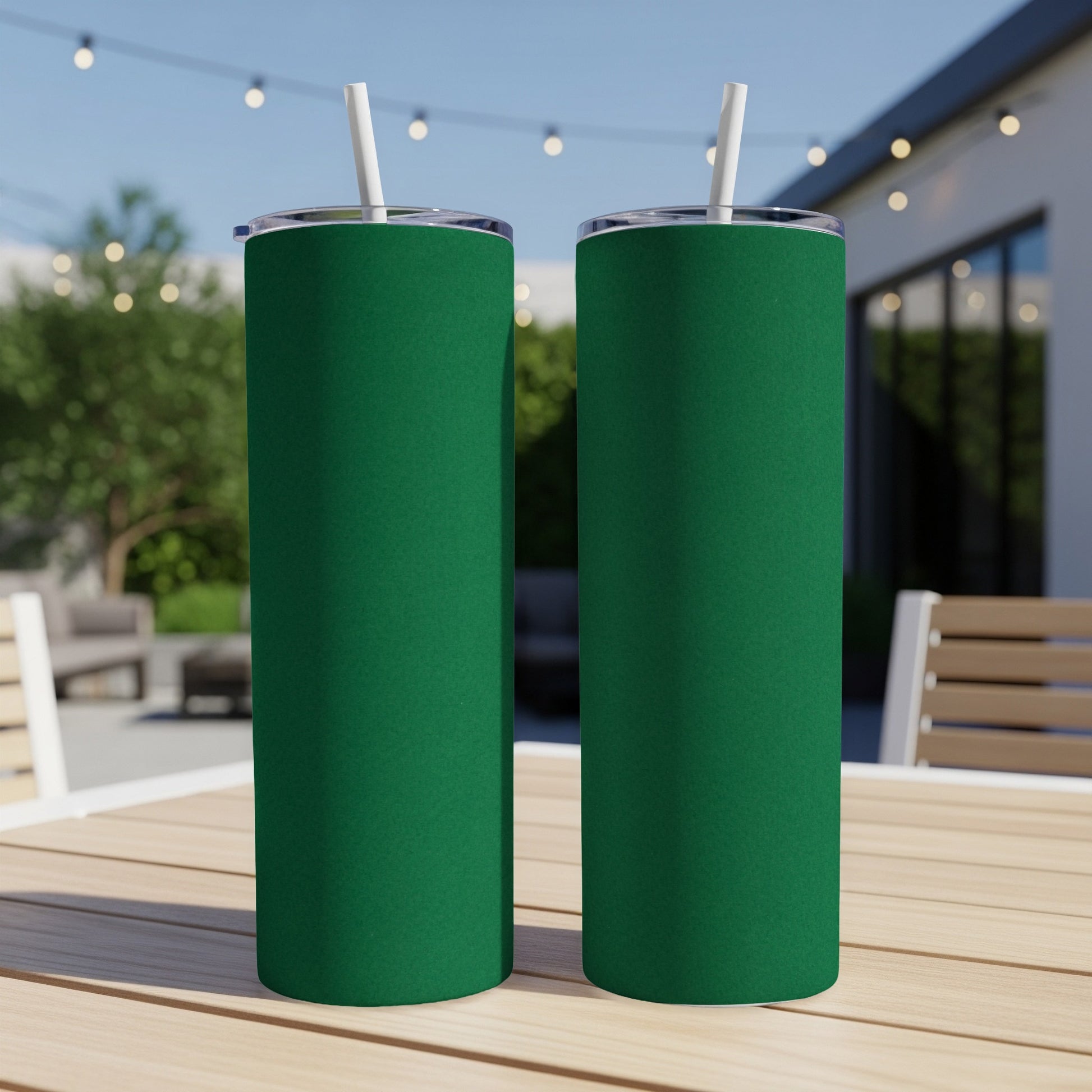 Two green tumblers with straws on a wooden table outdoors.