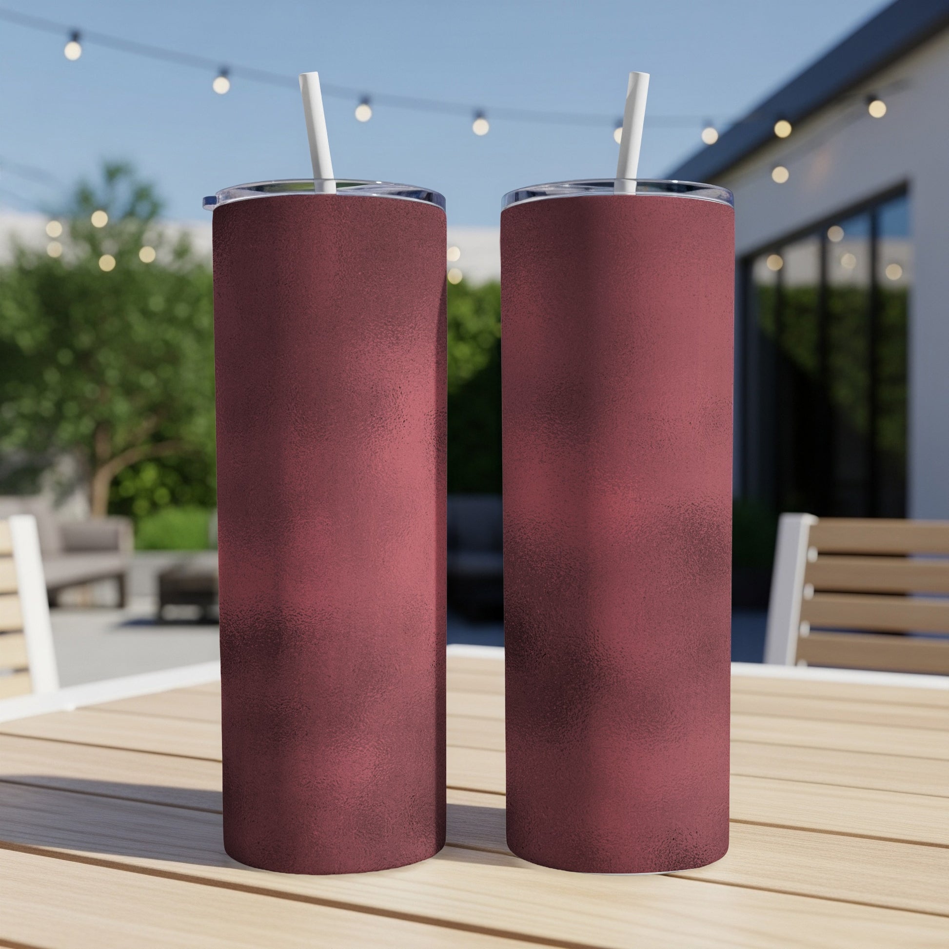 Two textured maroon tumblers with white straws sit on a wooden table.