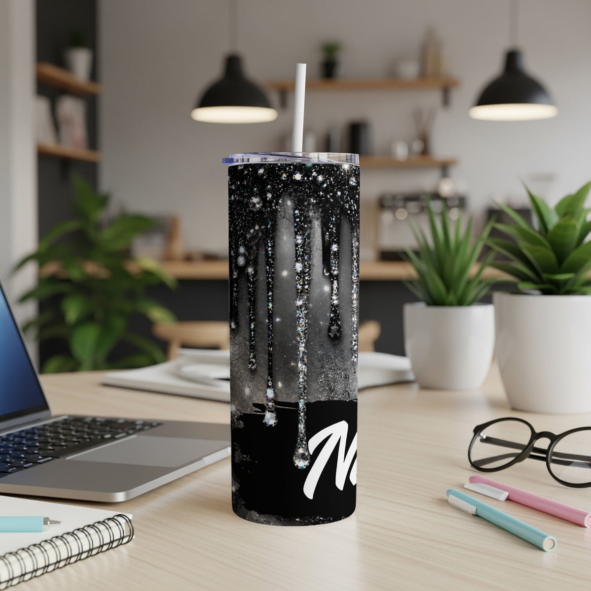 Black glitter tumbler with dripping rhinestones and a white "N" on a desk.