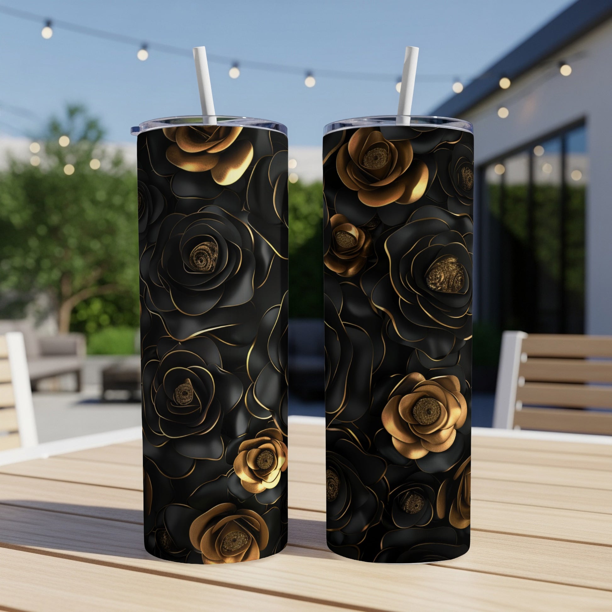Two black tumblers with gold floral designs sit on a table outdoors.
