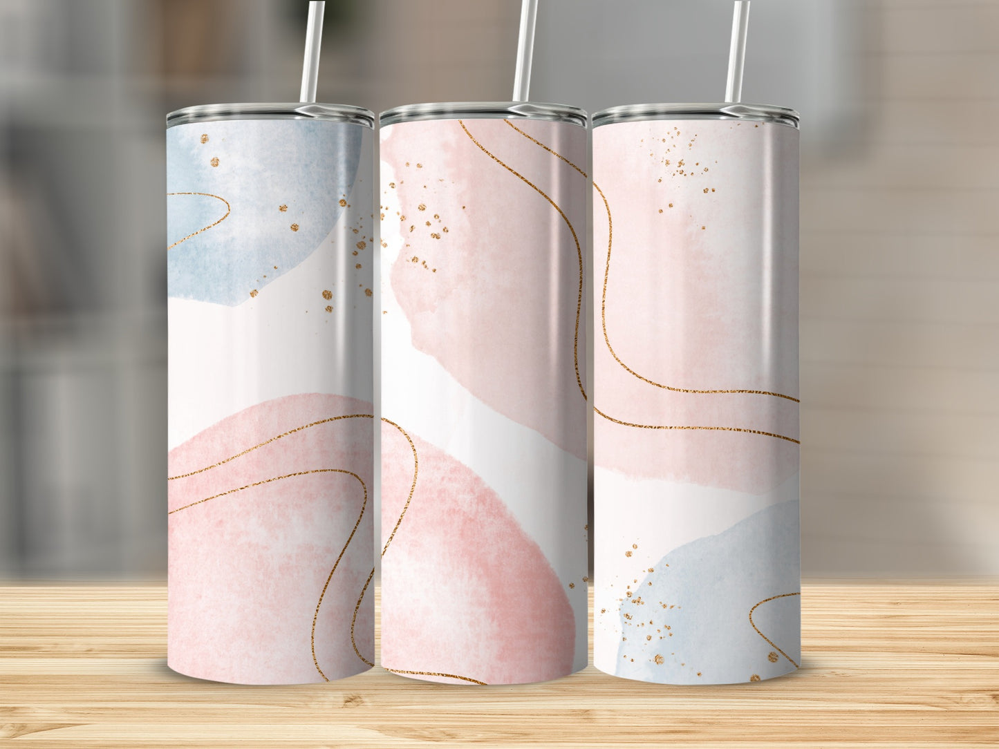 Three tumblers with abstract watercolor designs and gold accents on a wooden surface.
