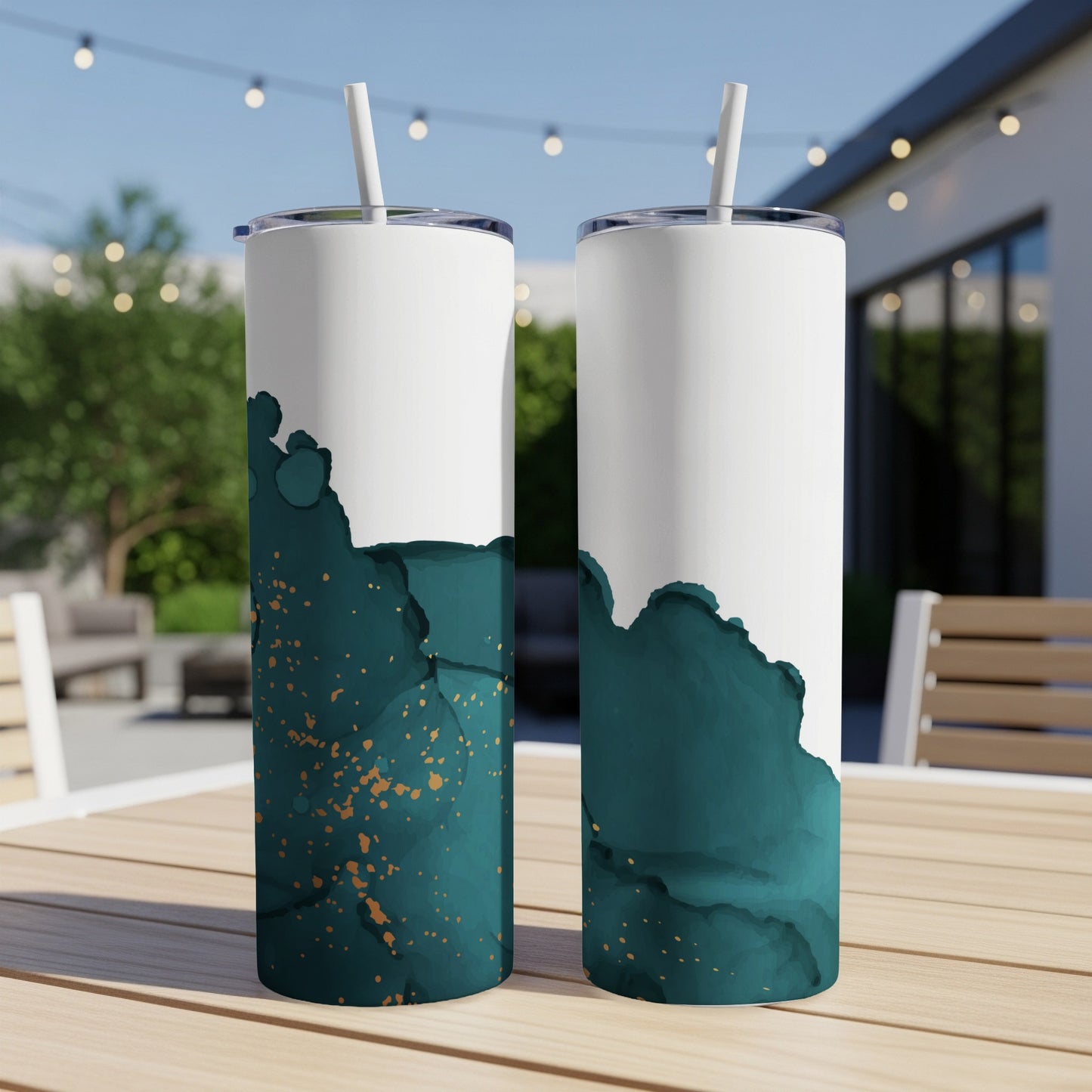 Two white tumblers with teal and gold abstract design on outdoor table.