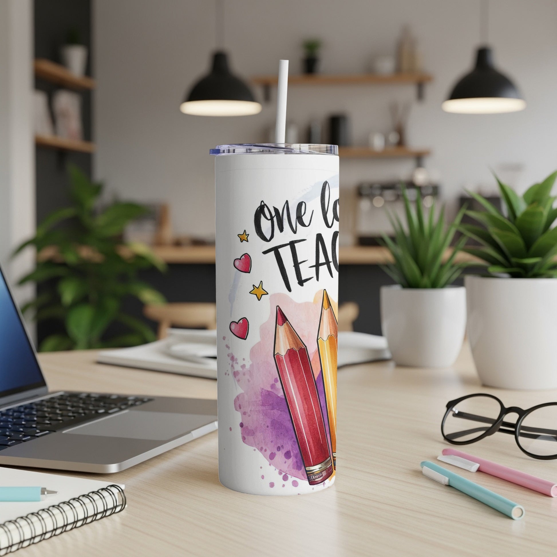 White tumbler with "One love teach" design and colorful pencils, on a desk.