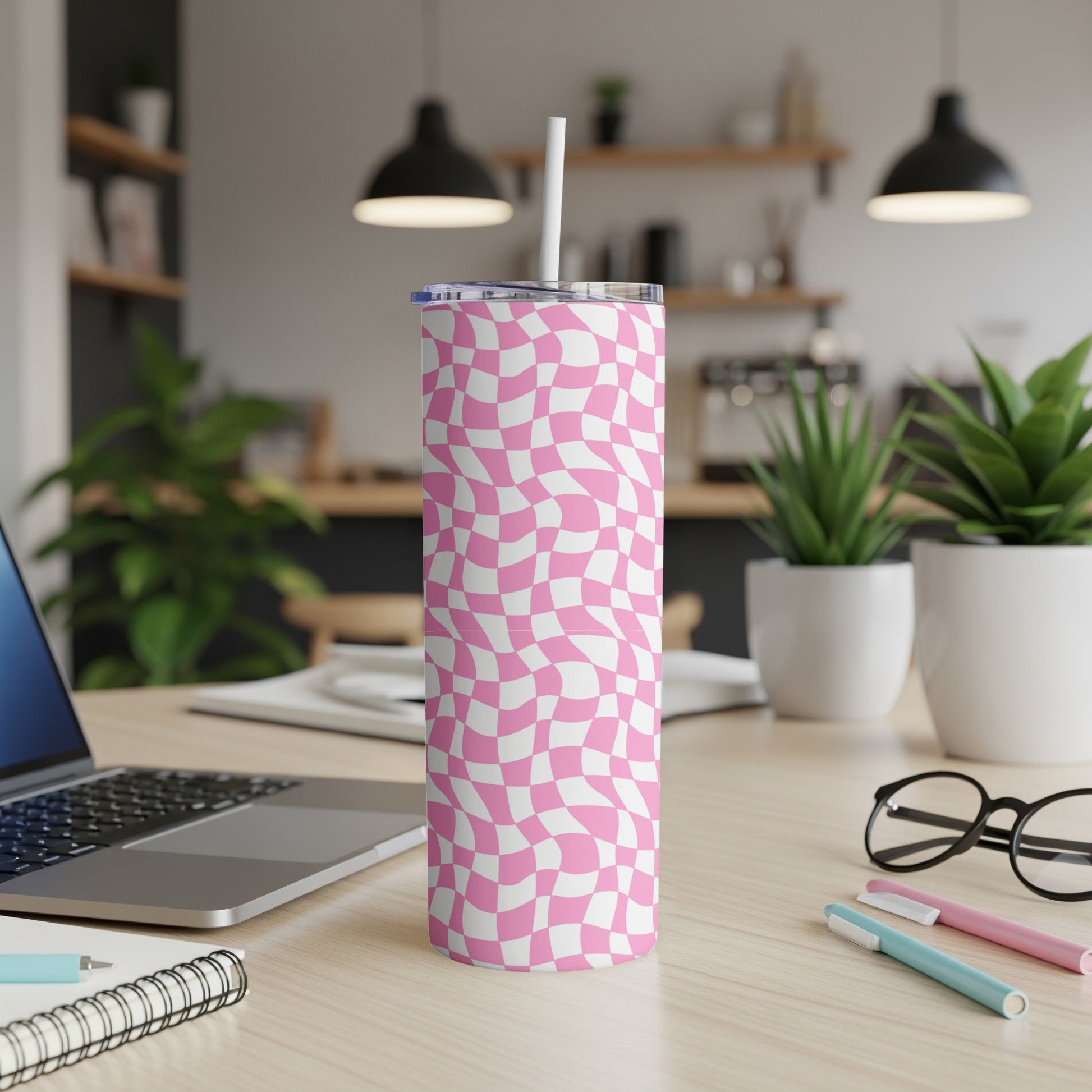 Pink and white checkered tumbler on a desk with a laptop.
