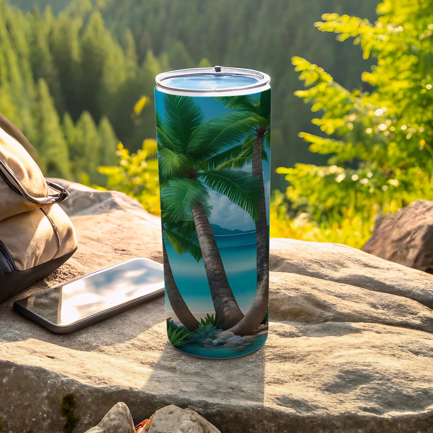 Tall tumbler with palm trees and ocean scene, resting on rocks outdoors.