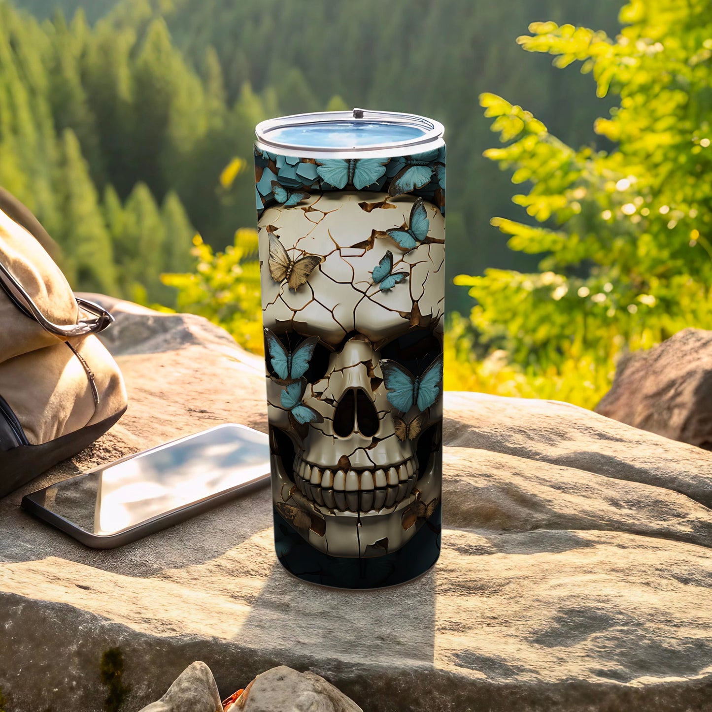 Skull and butterfly design on a tall tumbler beside a backpack and phone.