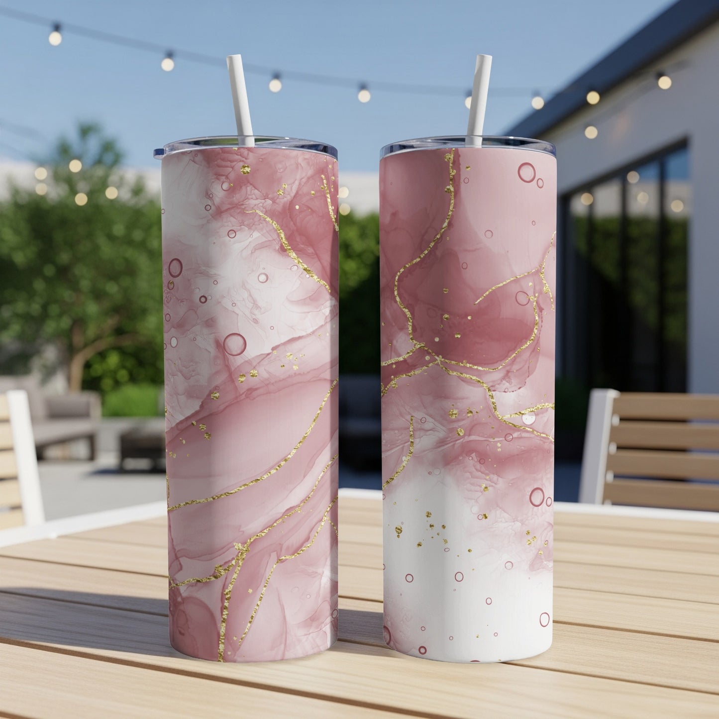 Two pink marble tumblers with gold veins on a wooden table outdoors.
