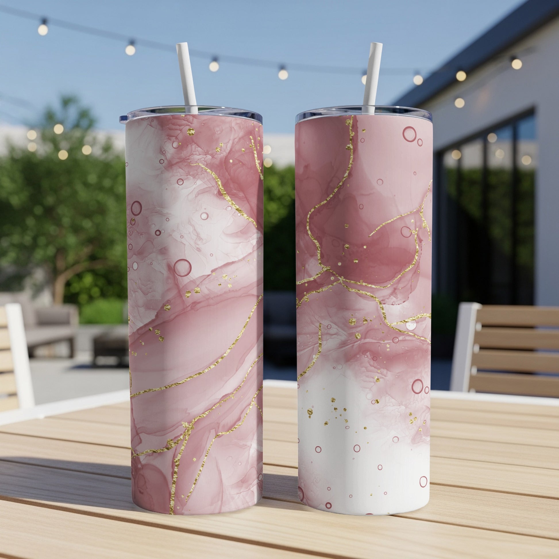 Two pink marble tumblers with gold veins on a wooden table outdoors.