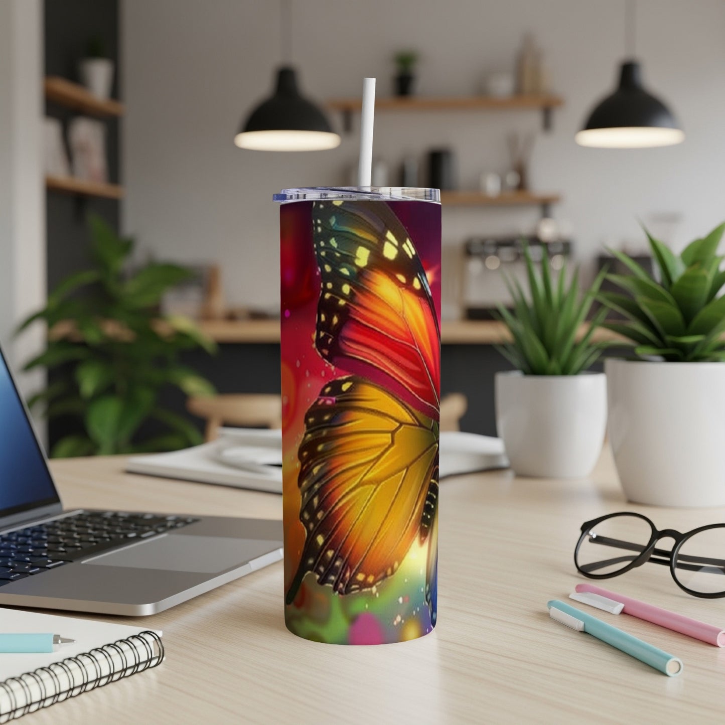 Butterfly tumbler with colorful wings on desk next to laptop and pens.